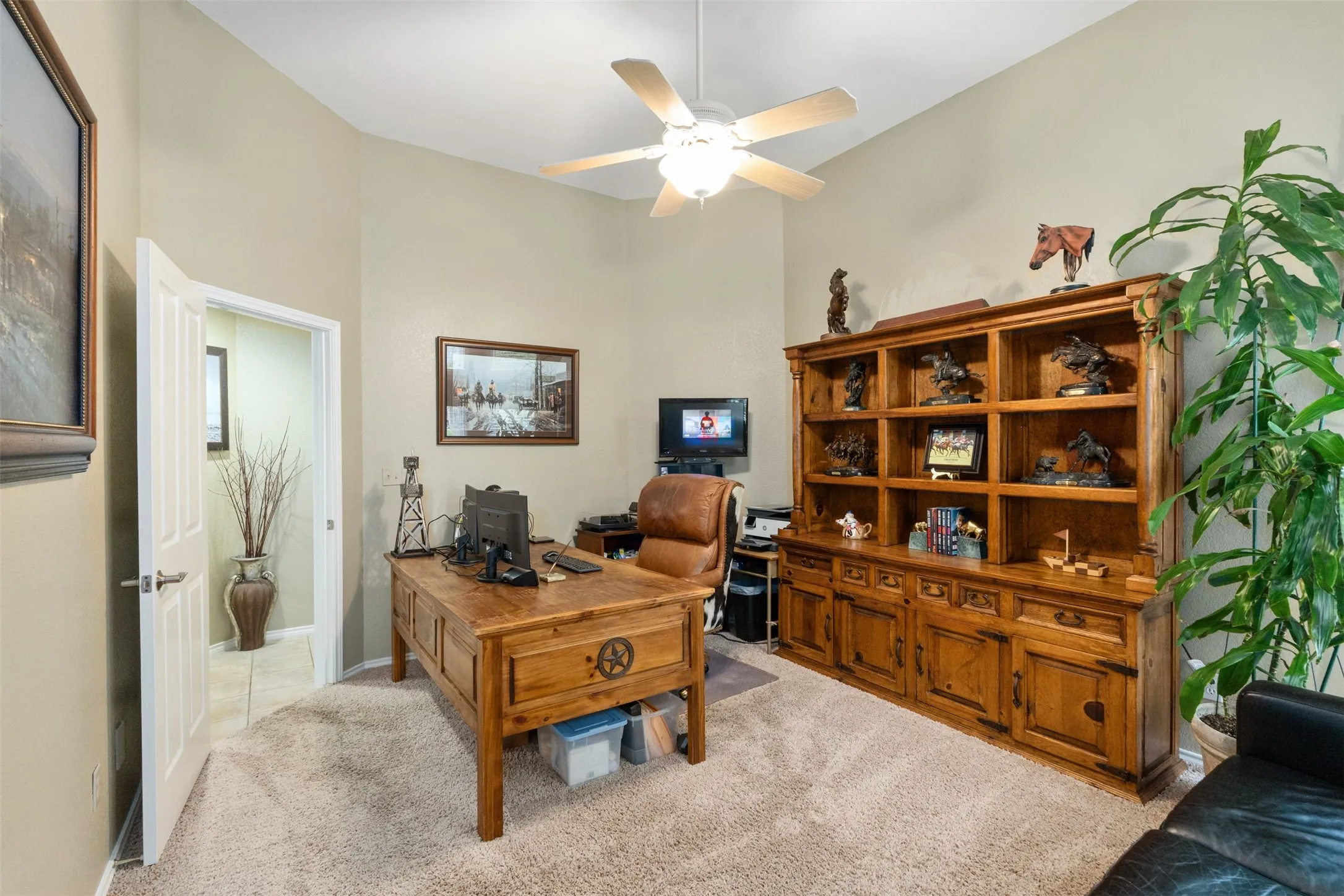Carpeted interior space featuring a ceiling fan with light fixture, neutral wall colors, an open doorway, and a built-in wooden shelving unit with lower cabinetry