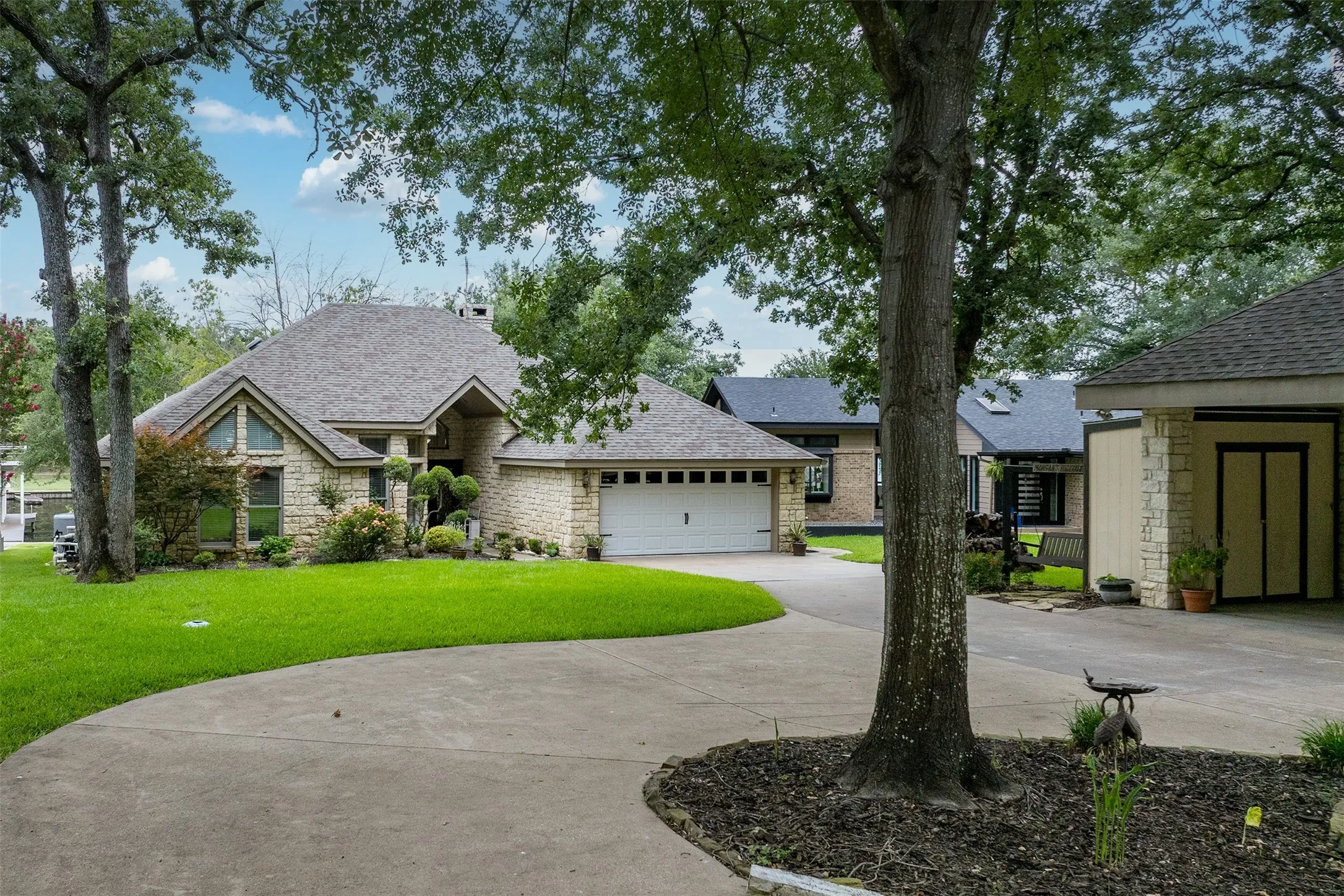 Stone-clad exterior featuring multiple gables, a two-car garage, and a curved concrete driveway