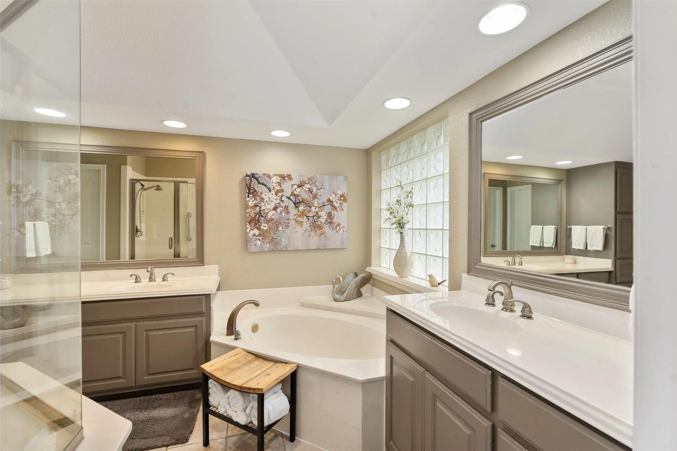 Bathroom featuring an oversized soaking tub, dual vanity with undermount sinks, glass block window, frameless glass shower enclosure, and recessed lighting
