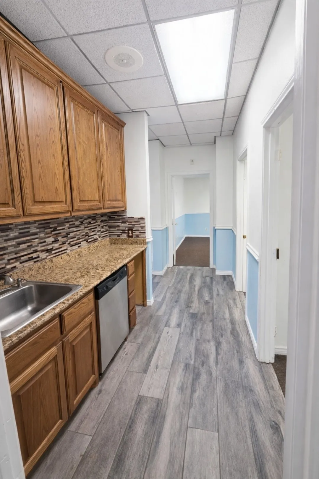 Galley-style kitchen featuring wood cabinetry, stainless steel sink, and a built-in dishwasher