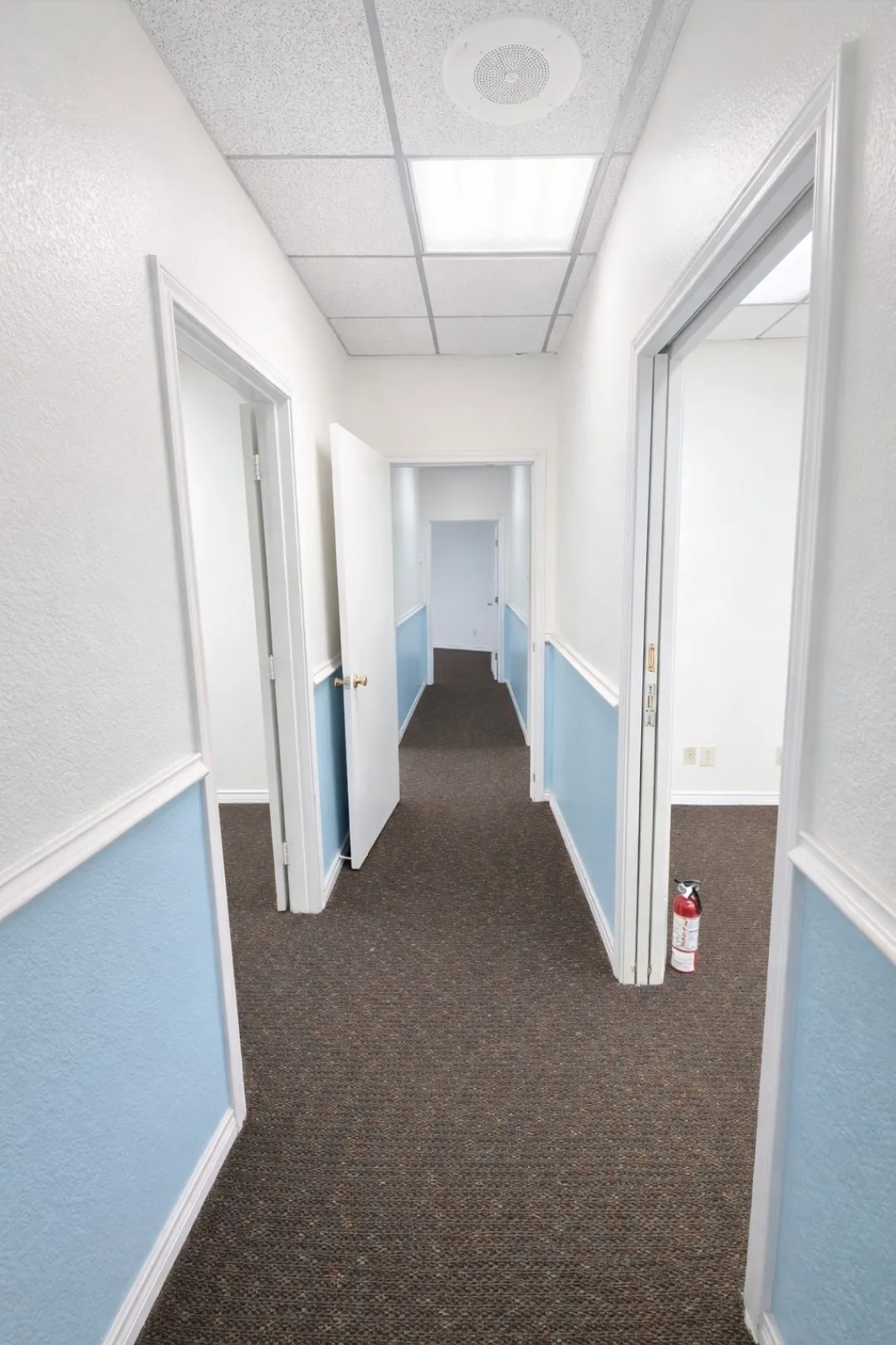 Hallway featuring drop ceiling with recessed lighting, brown carpet flooring, and white and blue textured walls