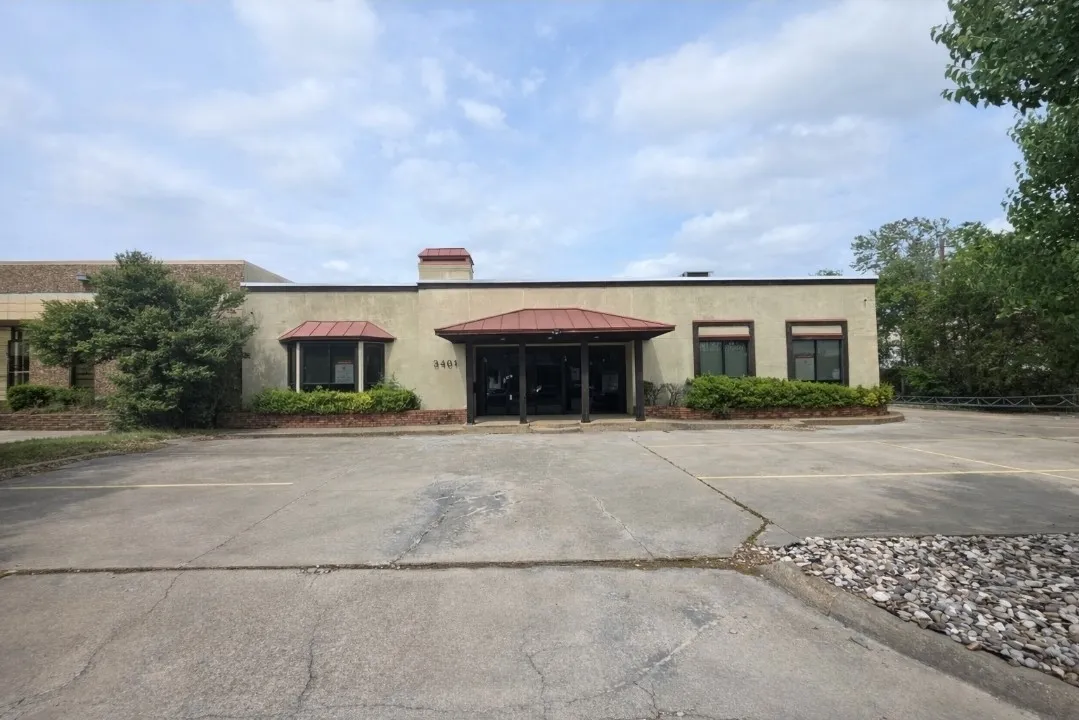 Exterior featuring a stucco finish, a covered entrance, a bay window with a red awning, and an asphalt parking area