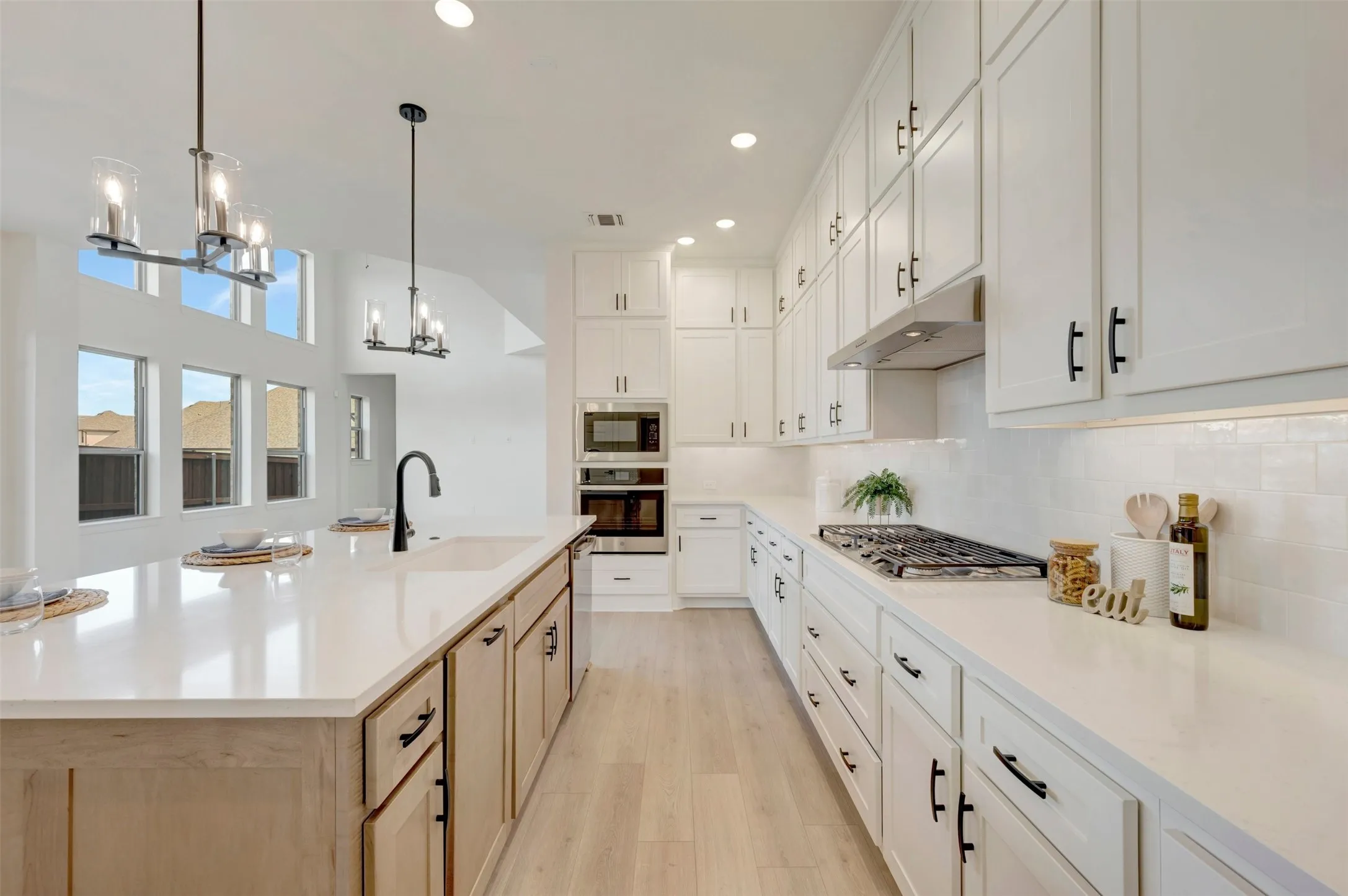 Kitchen featuring a gas range, built-in oven and microwave, white shaker cabinetry, an island with an integrated sink, and light wood-finish flooring