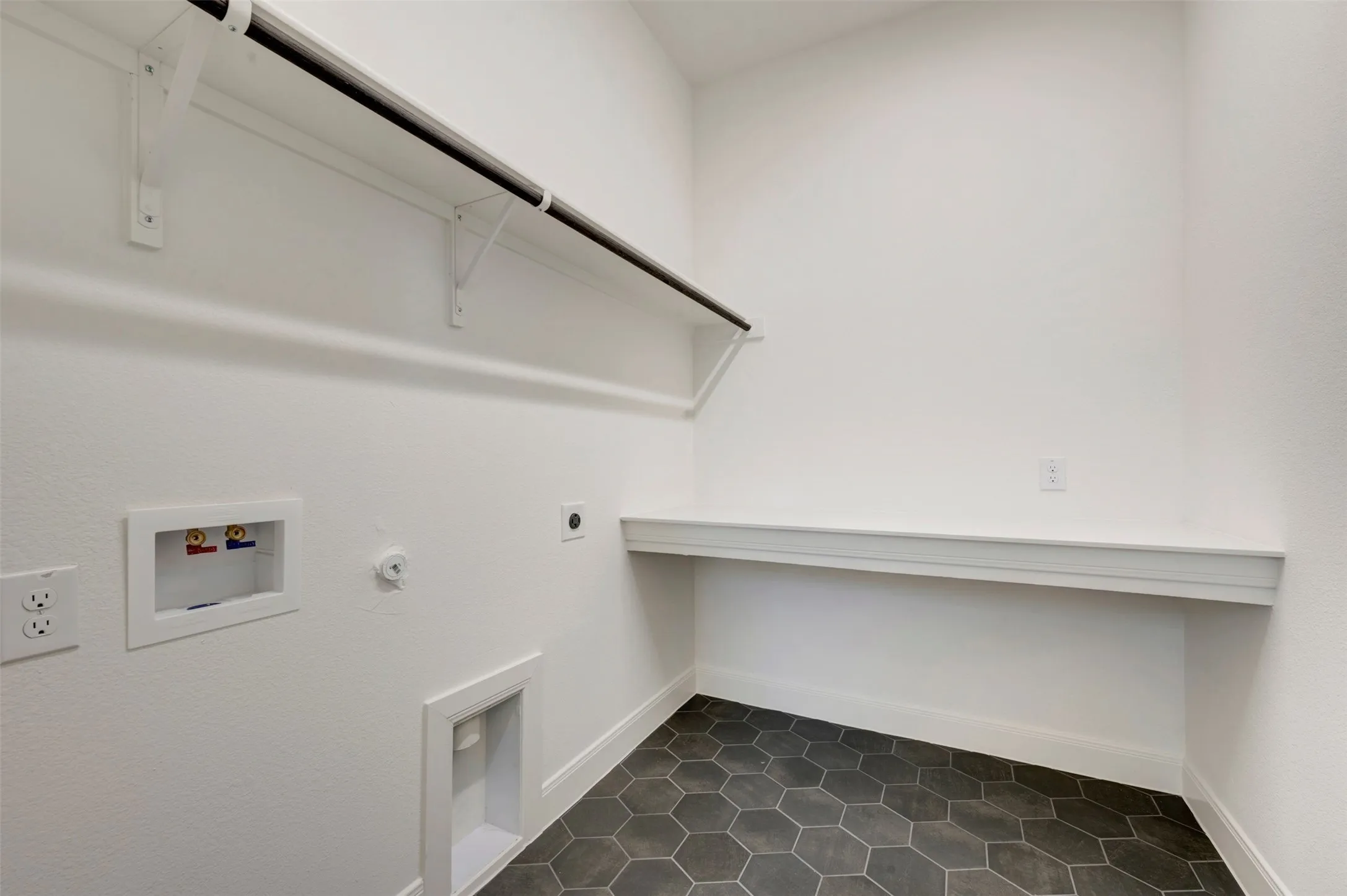 Hexagonal floor tiling, white walls, built-in shelving, white countertop, and laundry connections