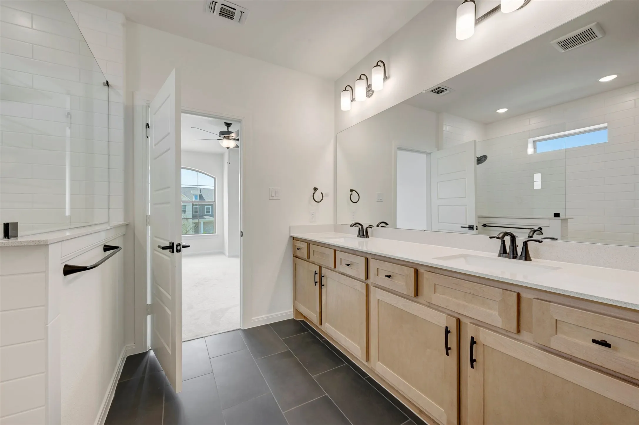Dual vanity with matte black fixtures, quartz countertops, natural wood-finish cabinetry, and dark tiled flooring