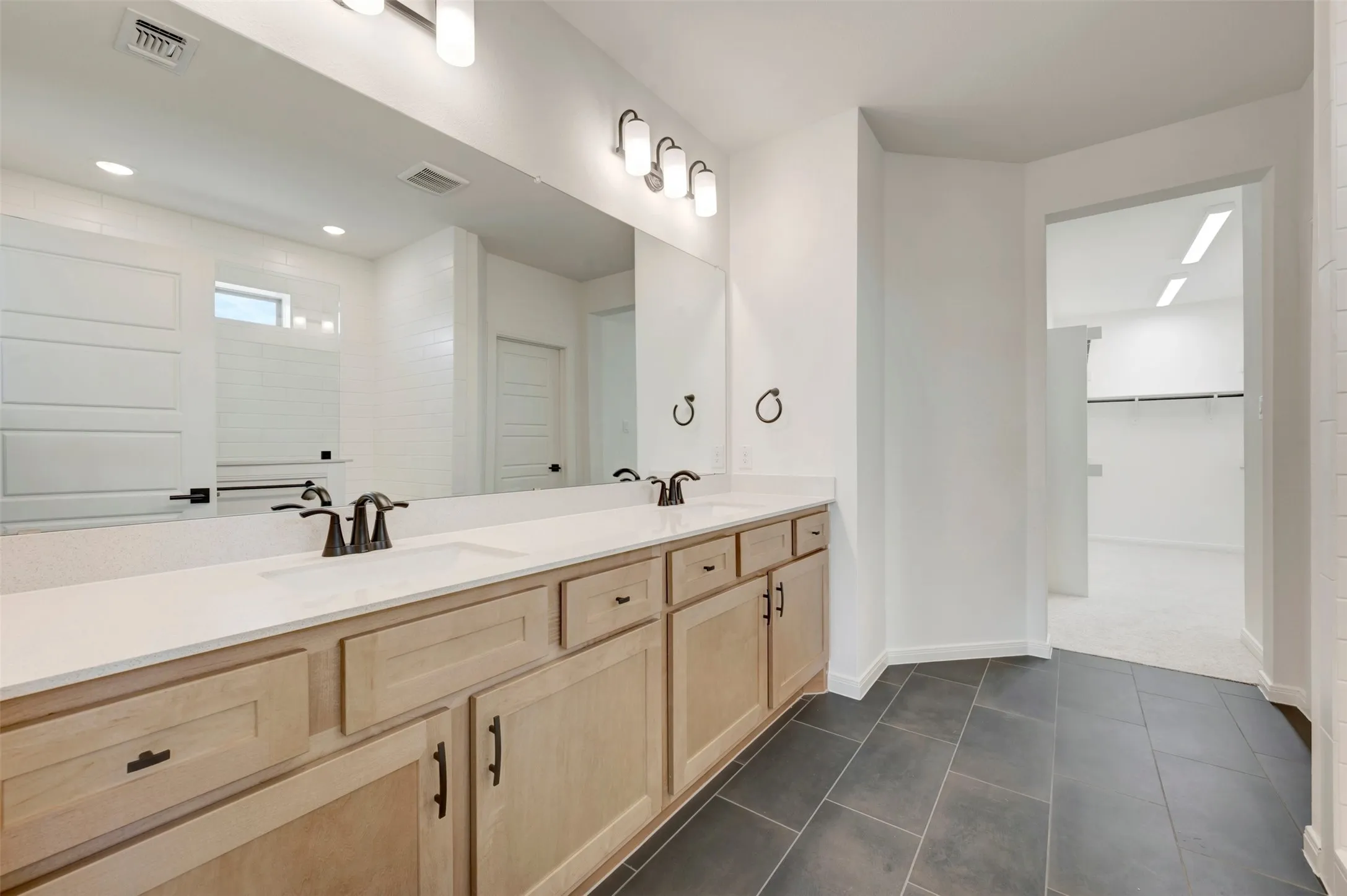 Double vanity with light wood-finish cabinetry, white countertop, and dark rectangular floor tiles