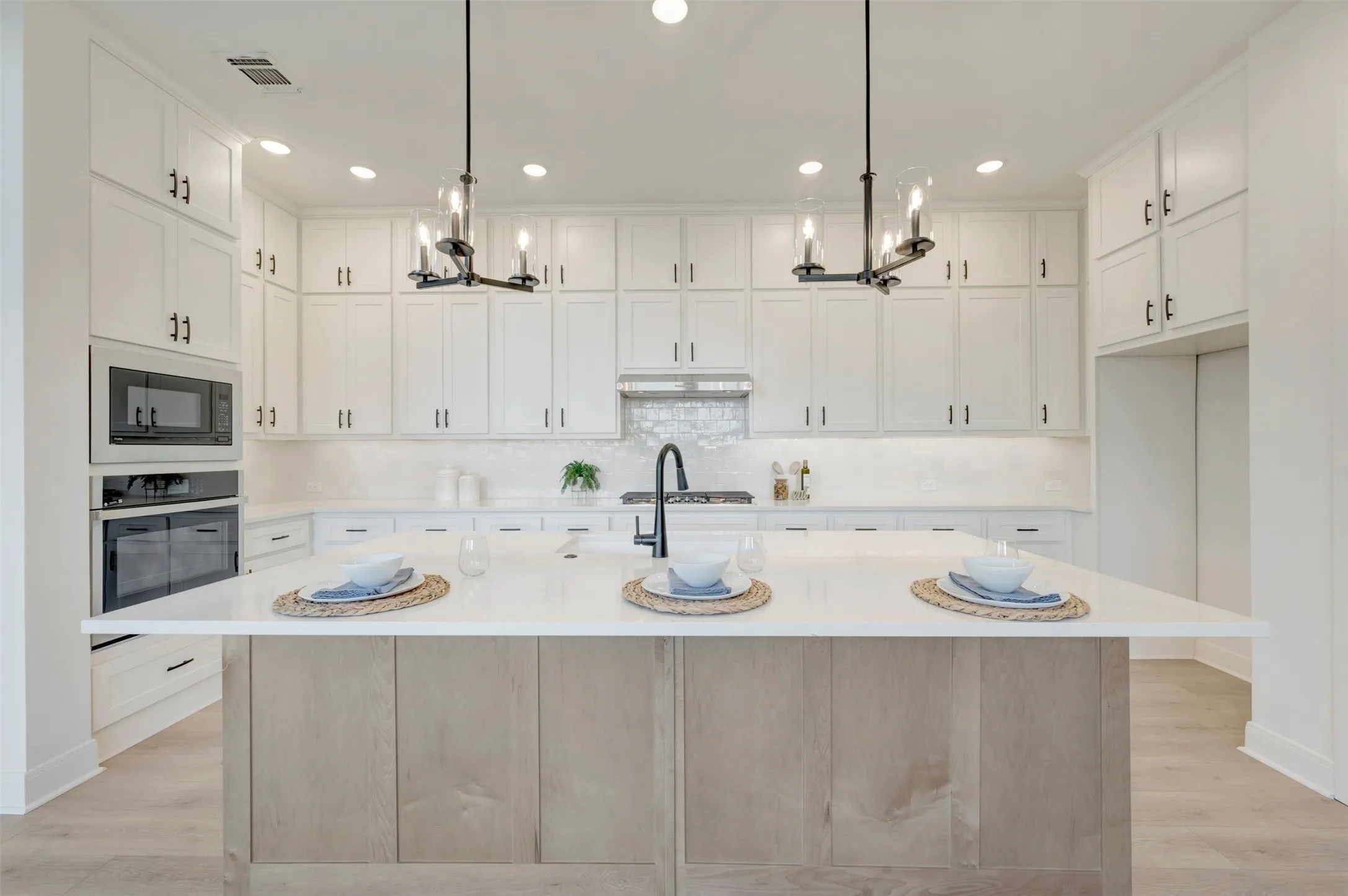 Spacious kitchen featuring white cabinetry, a large center island with a light wood-finish base, stainless steel appliances, and pendant lighting
