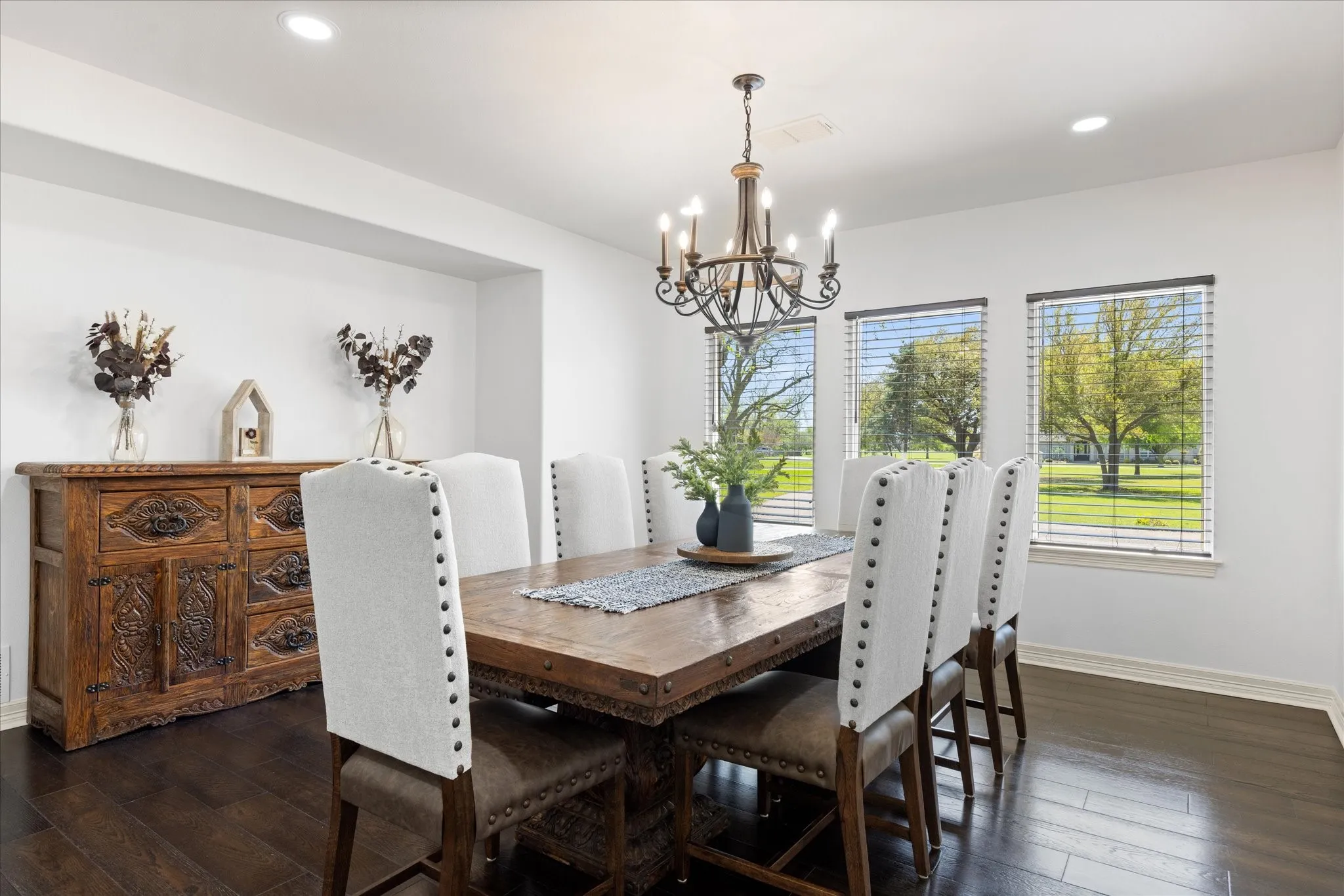 Dining area featuring dark wood-finish flooring, three windows with blinds, a recessed wall niche, and an ornate chandelier