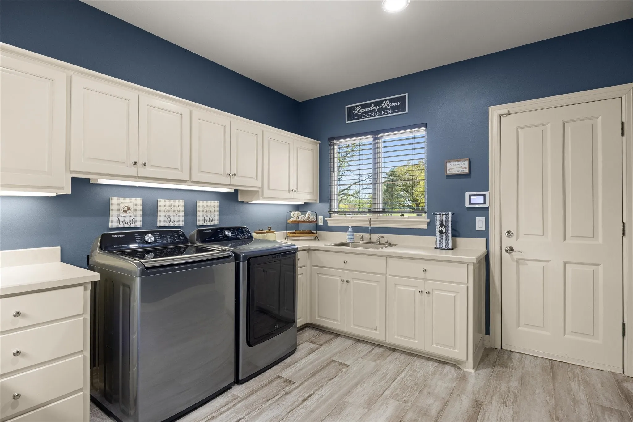Utility room featuring extensive cabinetry, undermount sink, light-toned countertops, wood-finish flooring, and a paneled entry door