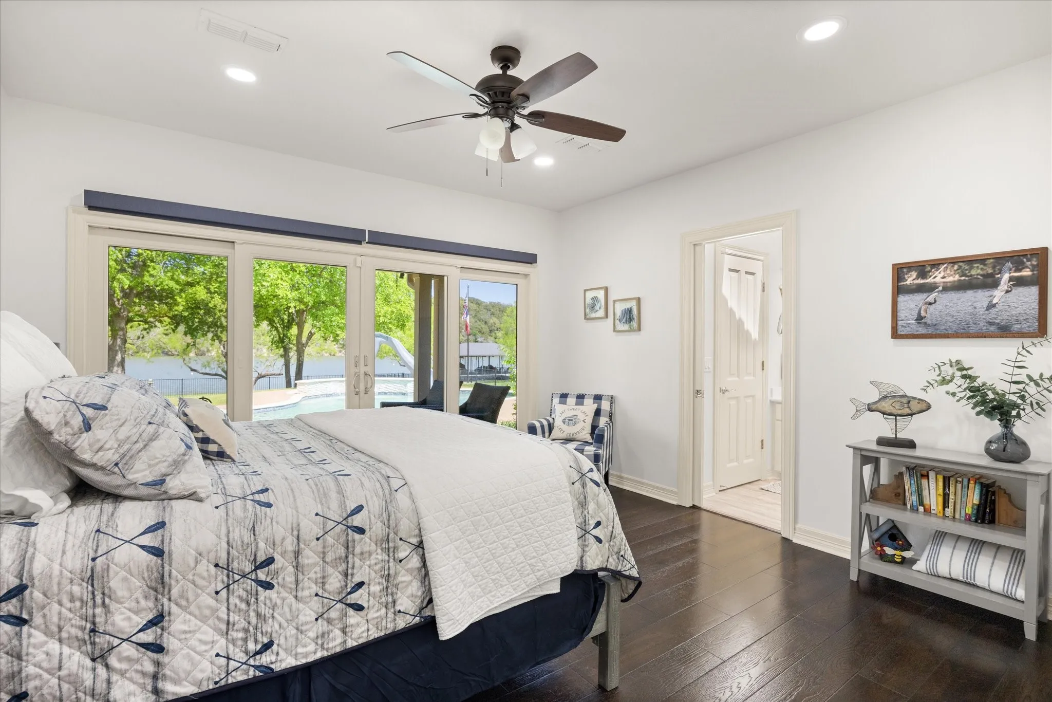 Spacious room featuring dark wood-finish flooring, a ceiling fan, recessed lighting, and a sliding glass door opening to an outdoor area with a pool and water body