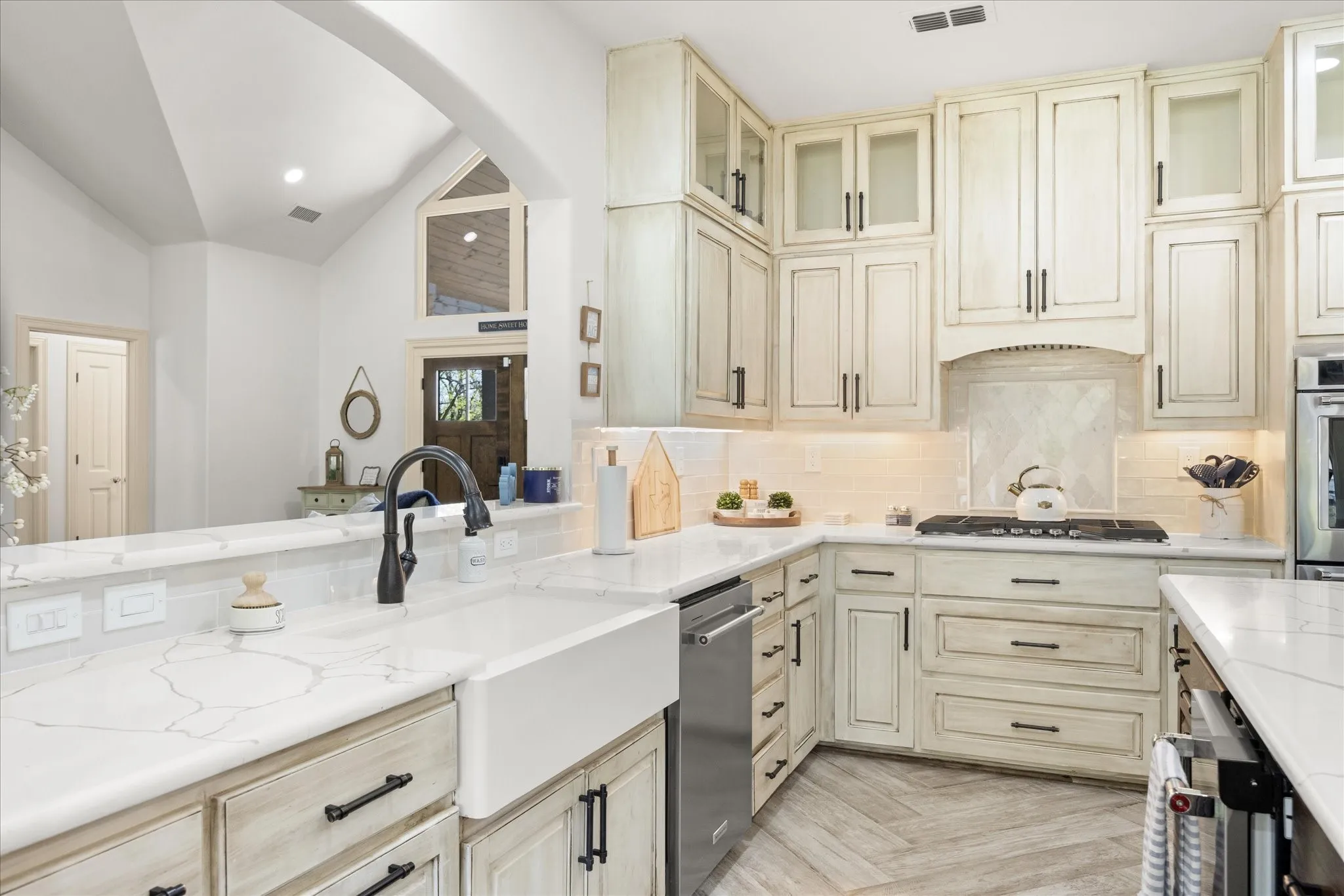 Gourmet kitchen featuring a farmhouse sink with a matte black faucet, light wood-finish cabinetry, stone countertops, a tile backsplash, and herringbone-patterned flooring