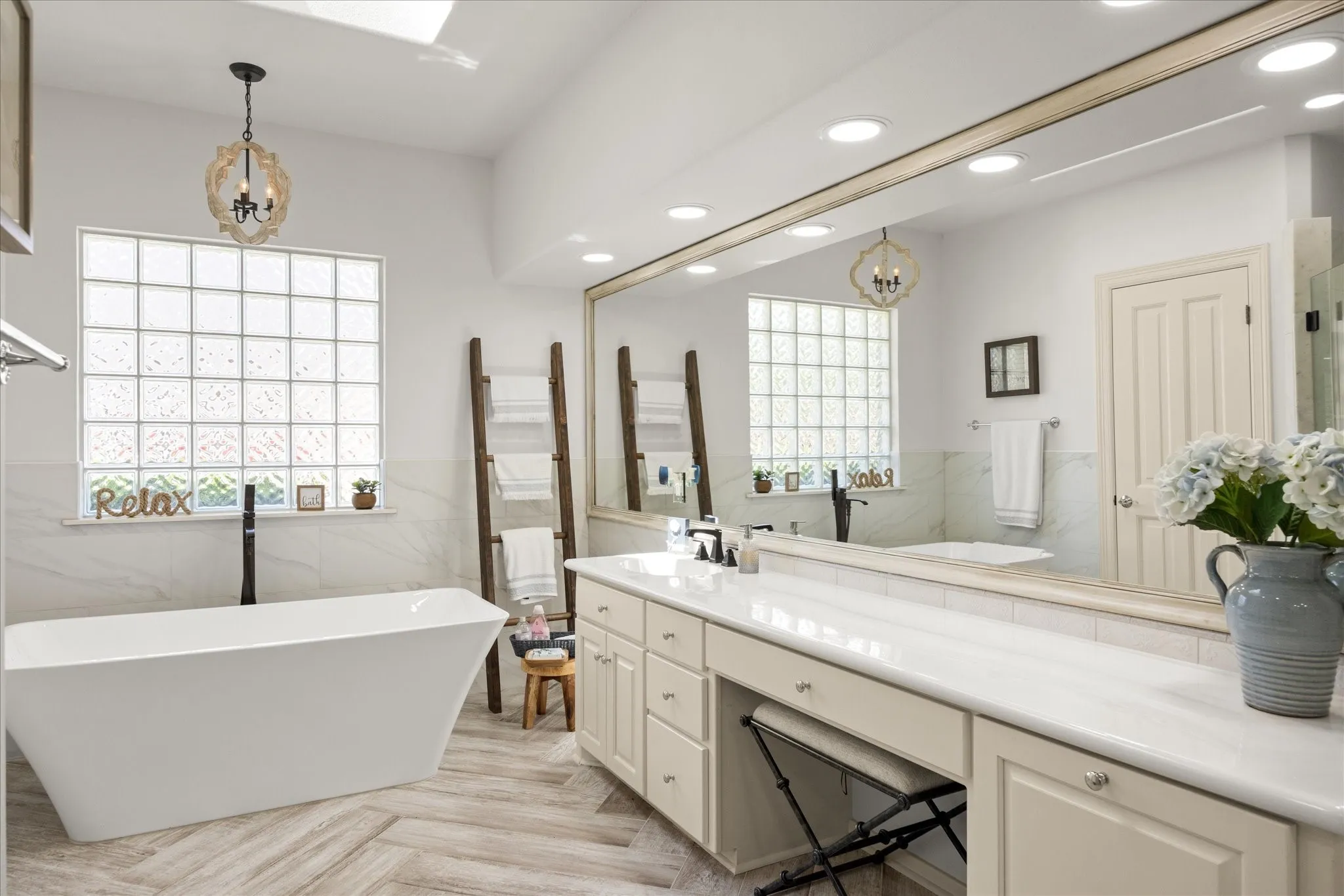 Spacious bathroom featuring a freestanding soaking tub, wood-finish herringbone flooring, and a large vanity with an integrated dressing area