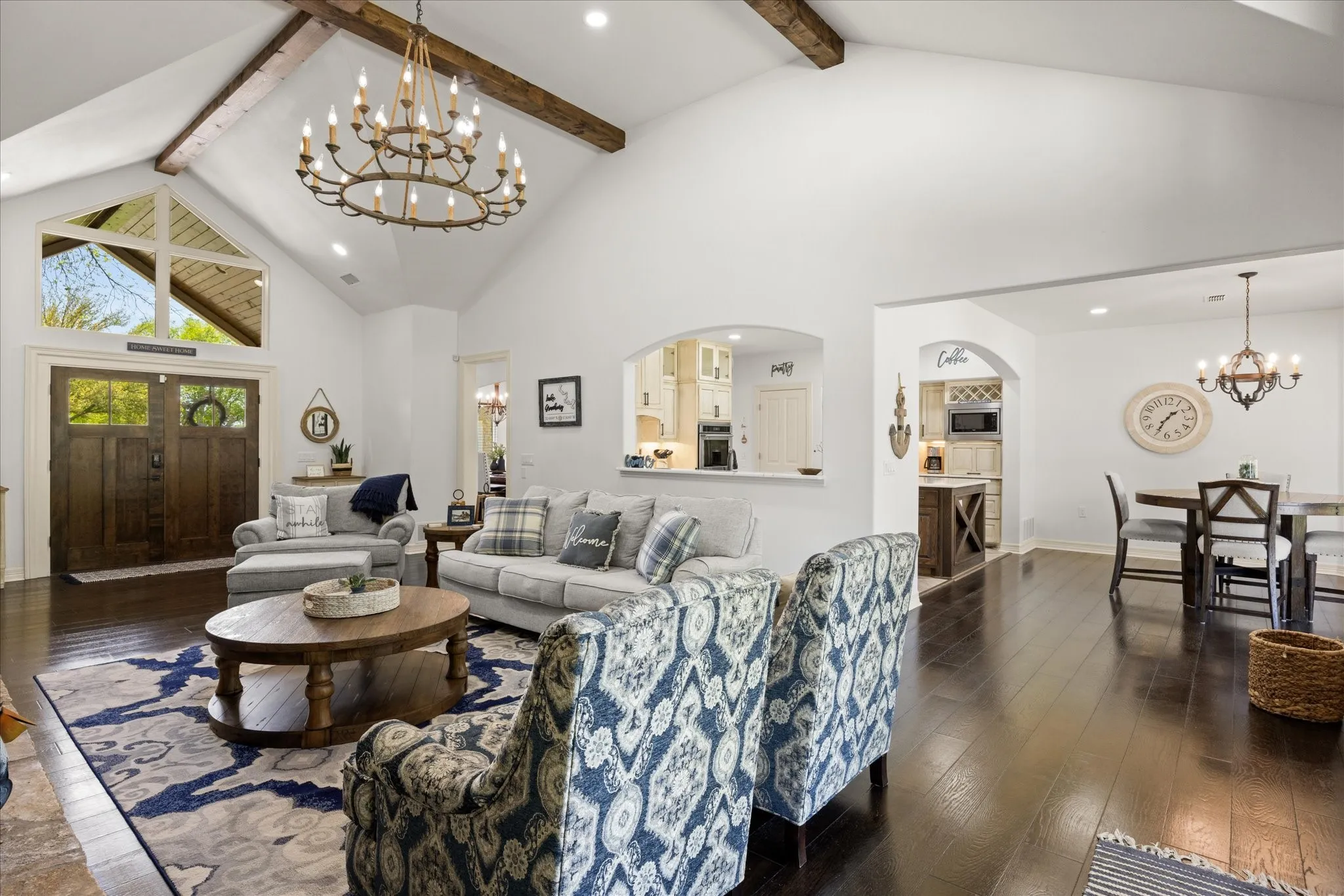 Spacious living area featuring vaulted ceilings with exposed wood beams, dark wood-finish flooring, a grand chandelier, and an arched entryway
