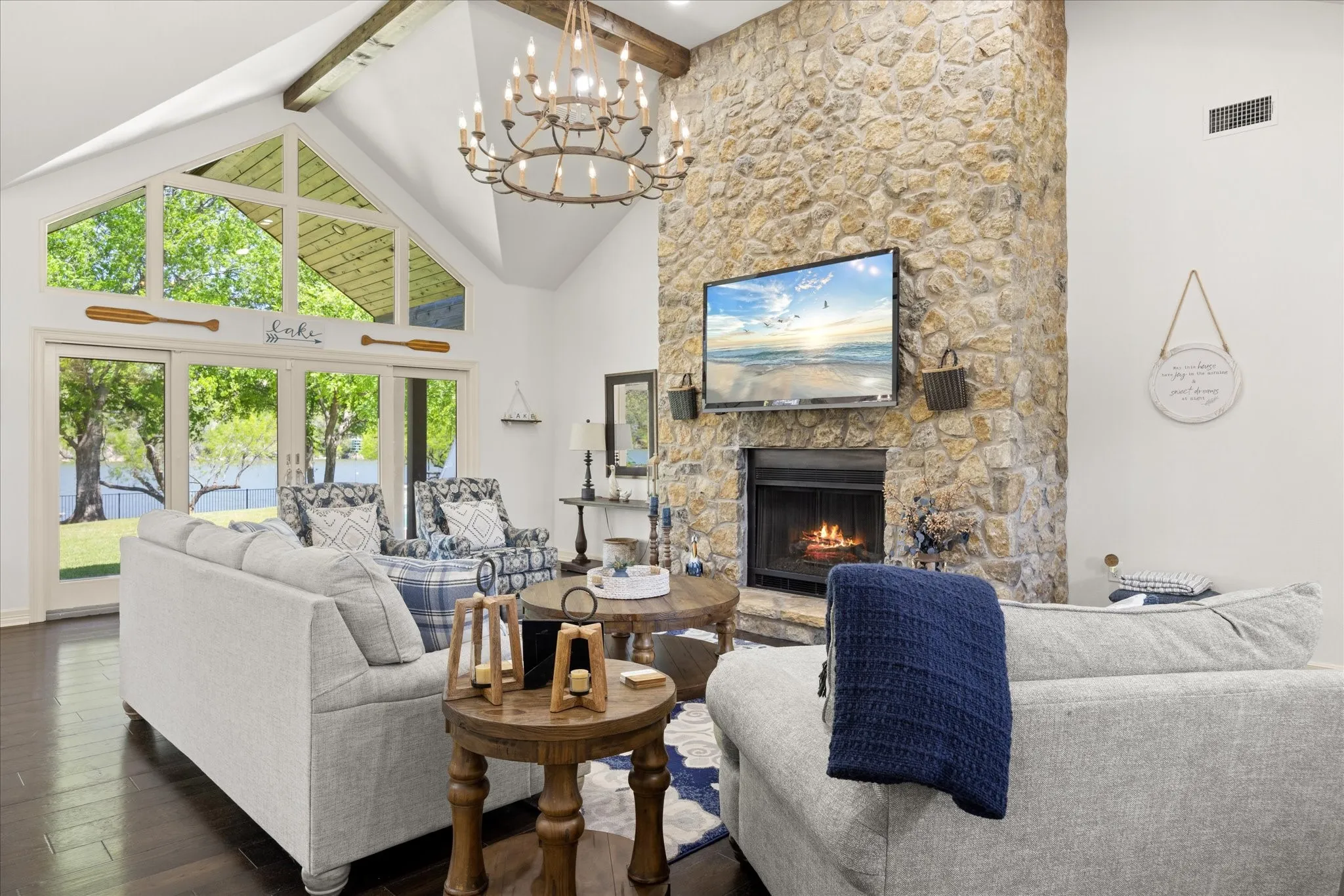 Expansive living area featuring a vaulted ceiling with exposed wood beams, a large stone fireplace, and dark wood-finish flooring