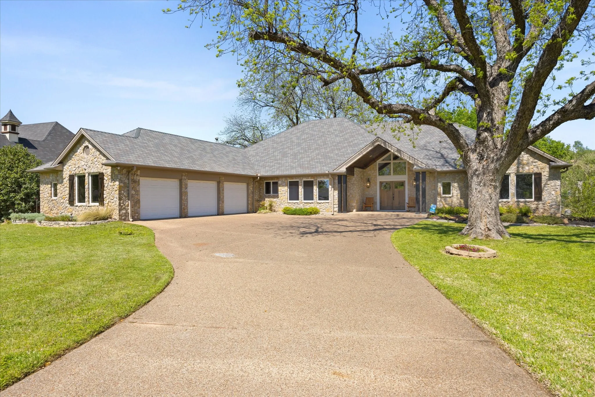 Stone exterior residence featuring a three-car garage, pitched roofline, and a prominent front entrance with a gabled accent