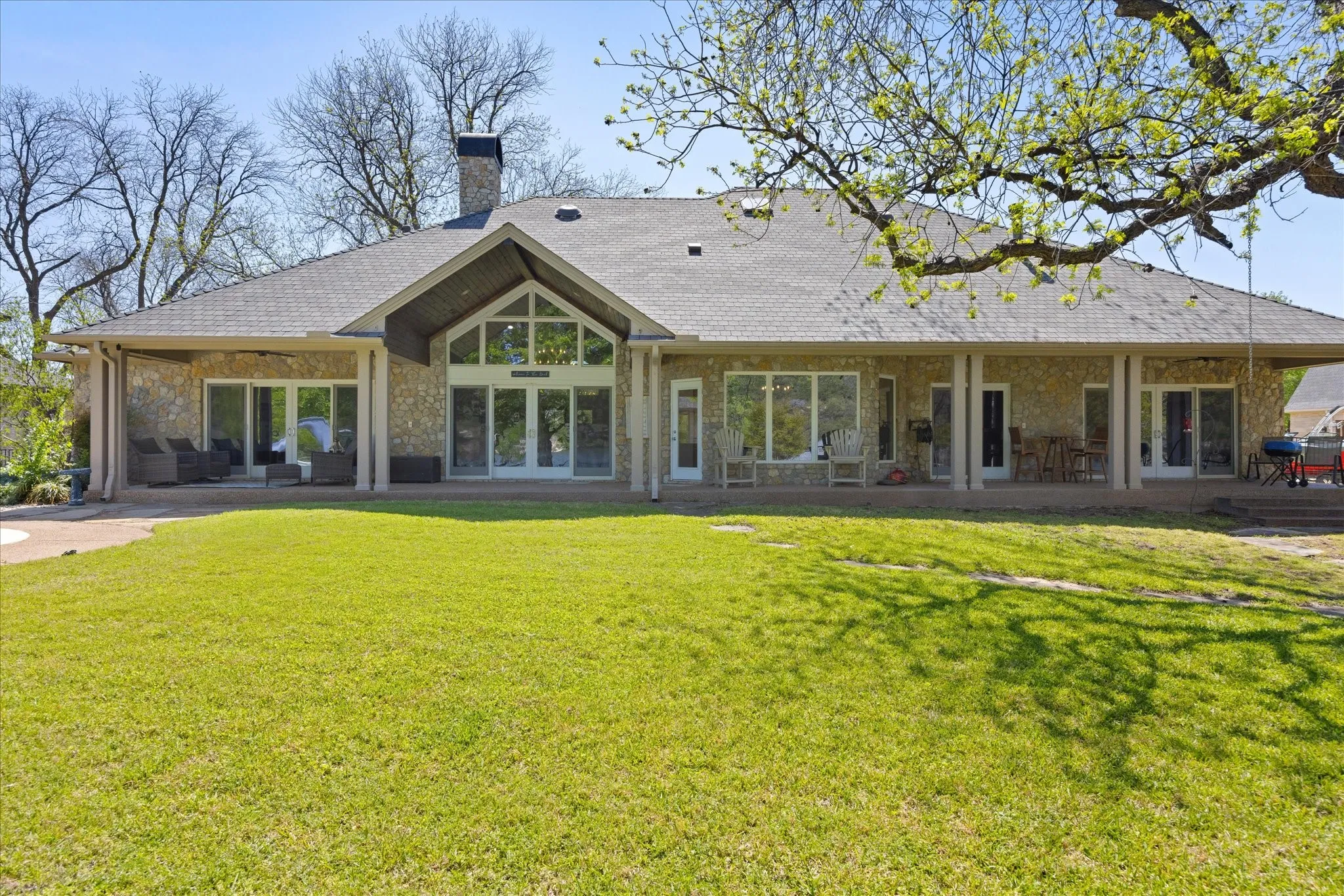 Stone exterior with an expansive covered patio, featuring multiple access points and a vaulted central window wall