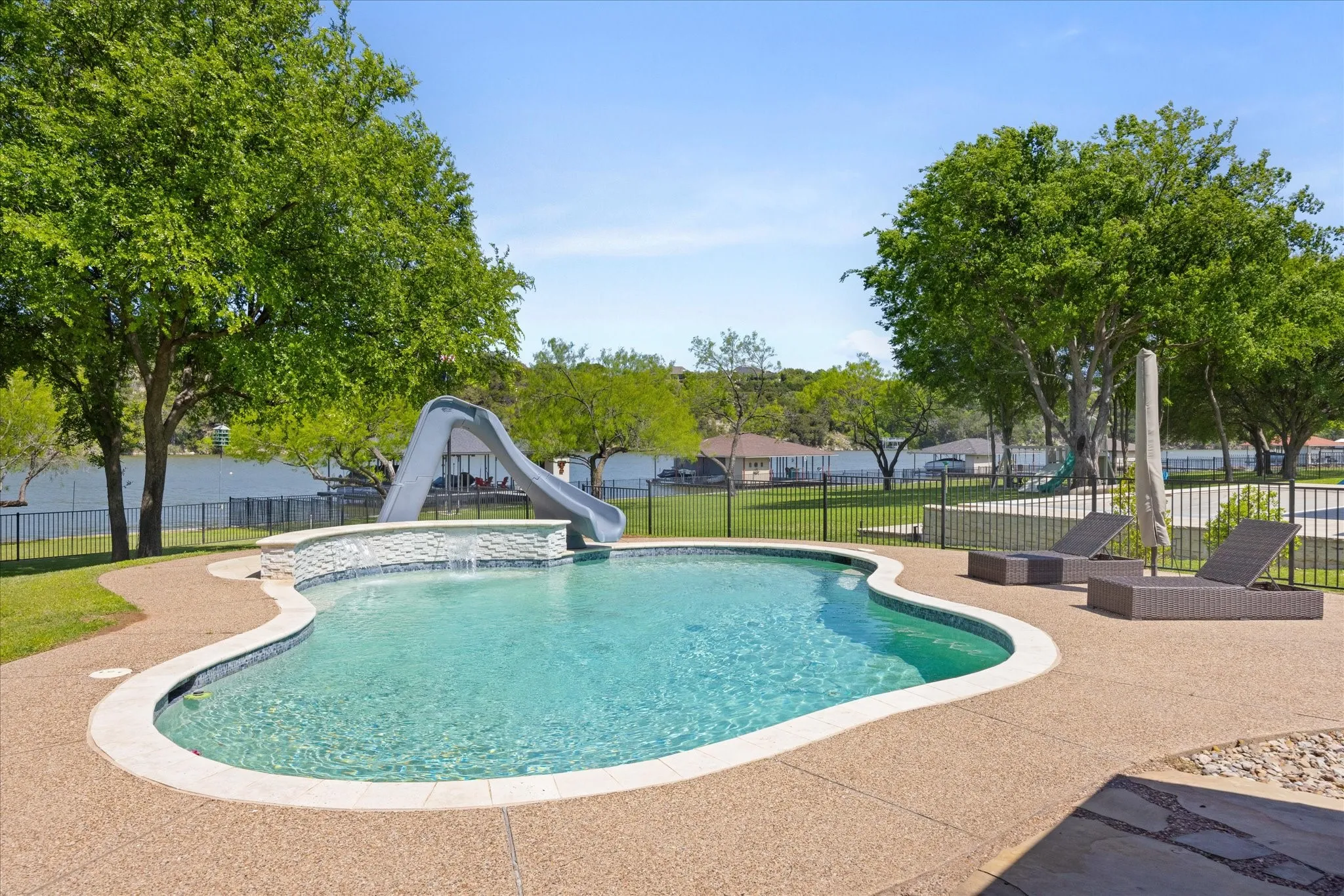 Freeform swimming pool featuring a waterfall, integrated slide, and expansive aggregate decking