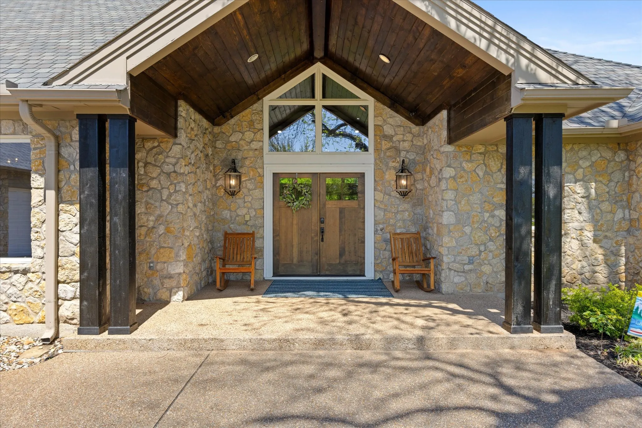 Stone façade entrance featuring a prominent gable window, dark wood-finish double doors, and complementary black support pillars