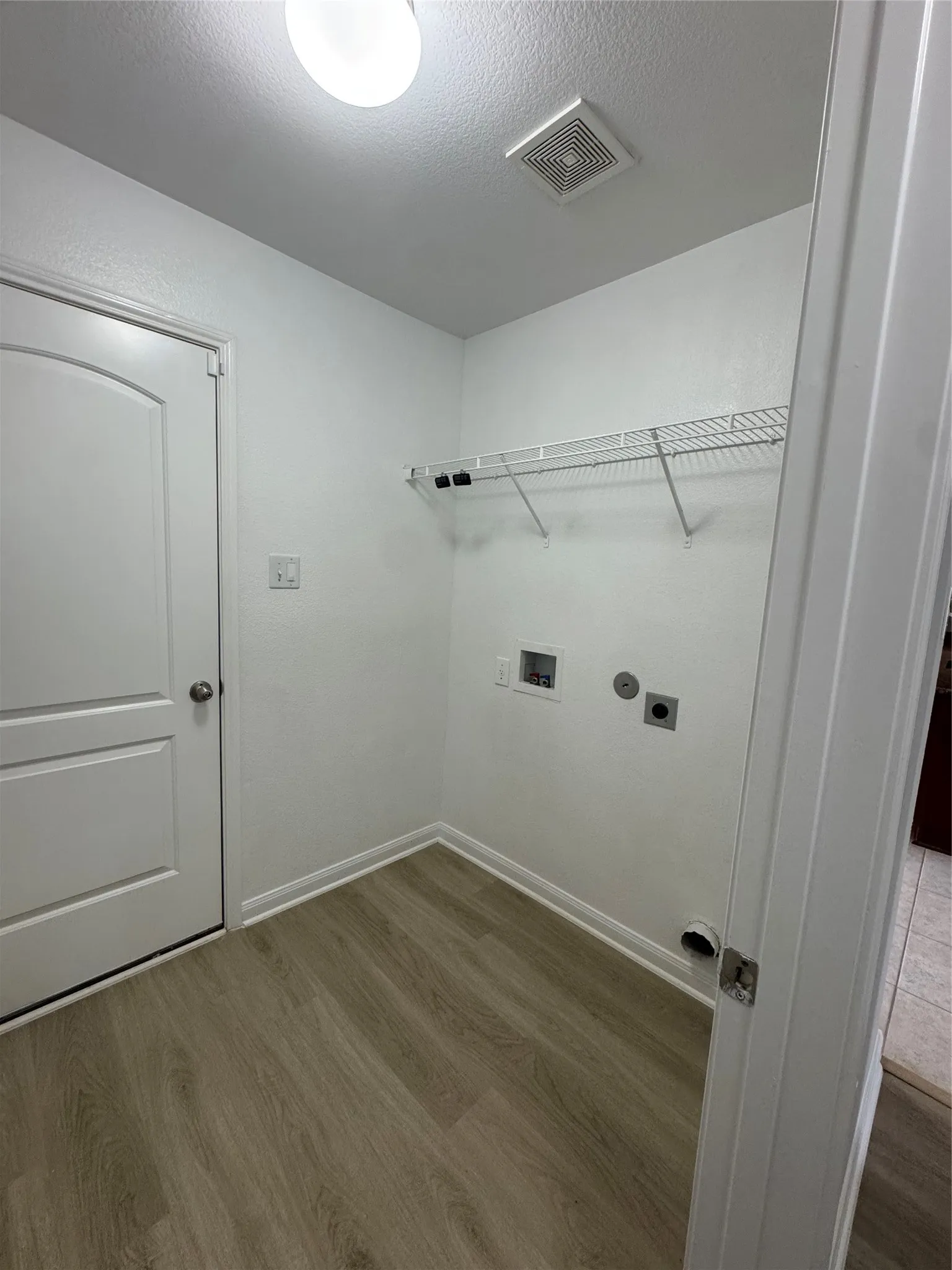 Dedicated utility space featuring wood-finish flooring, white walls, and a wire shelving unit