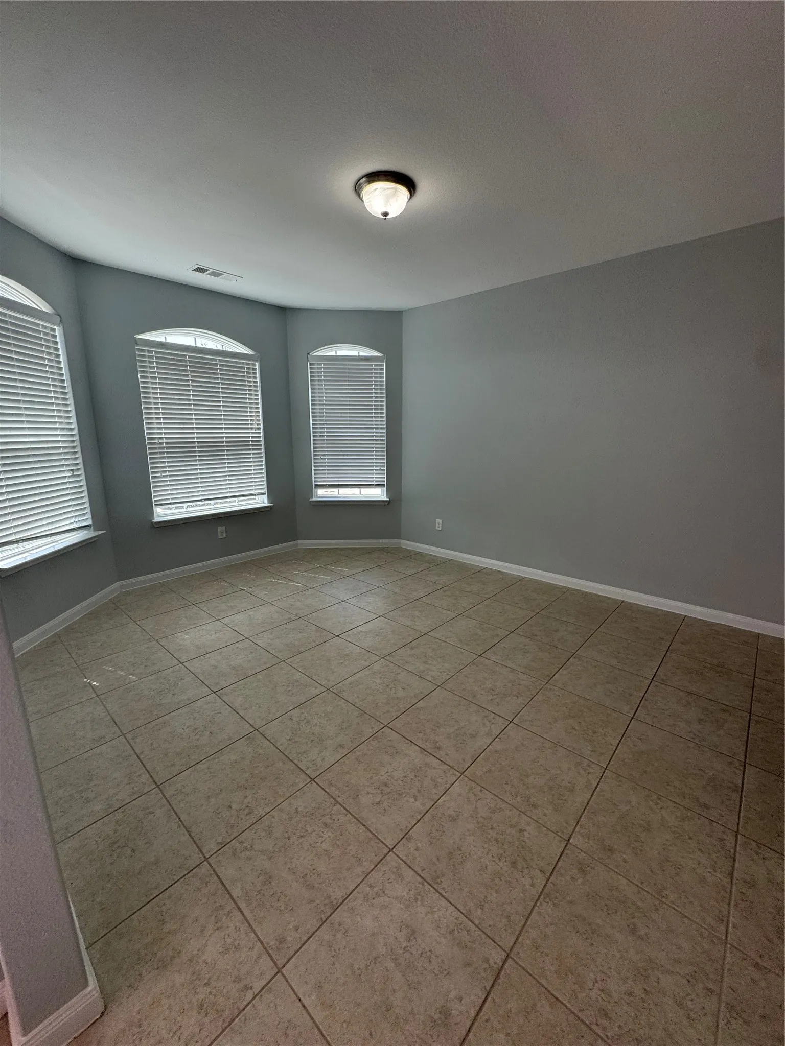 Spacious room featuring neutral tile flooring, light gray walls, and arched windows with blinds