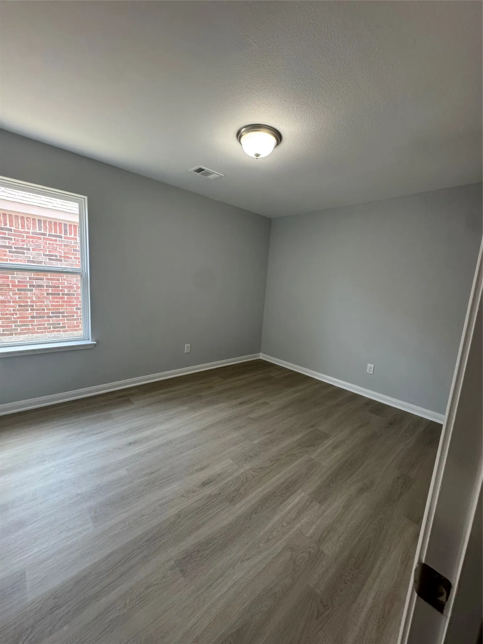 Room featuring light gray walls, wood-finish flooring, a contemporary ceiling light fixture, and white baseboards