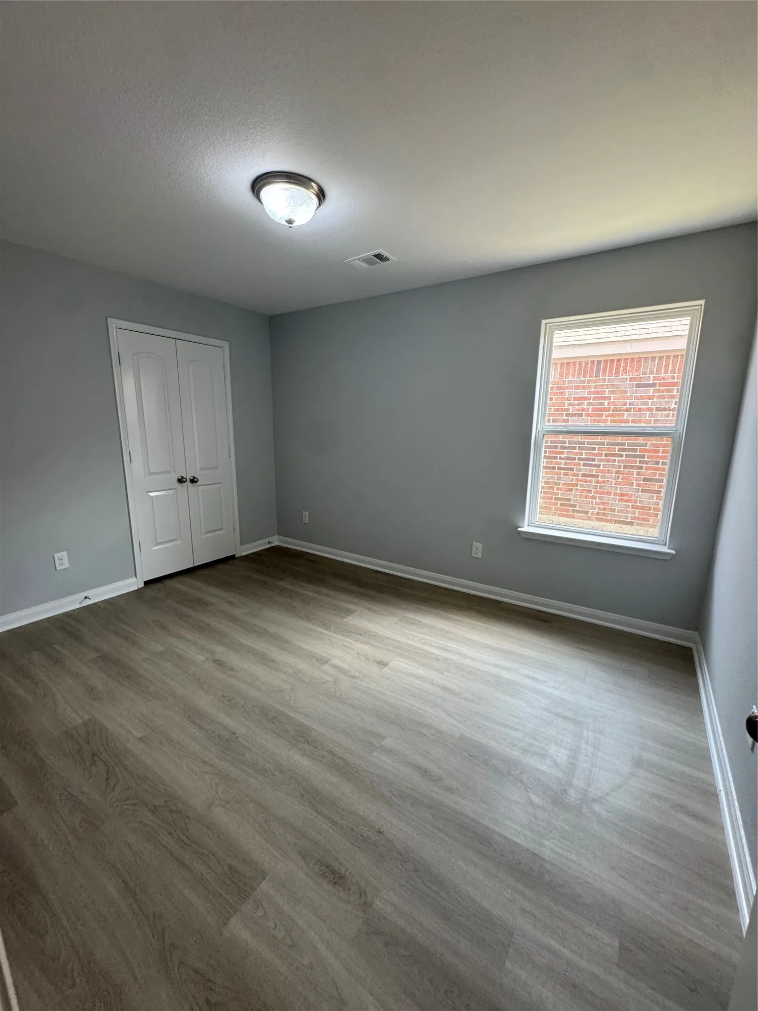 Spacious room featuring wood-finish flooring, light grey walls, and a large window