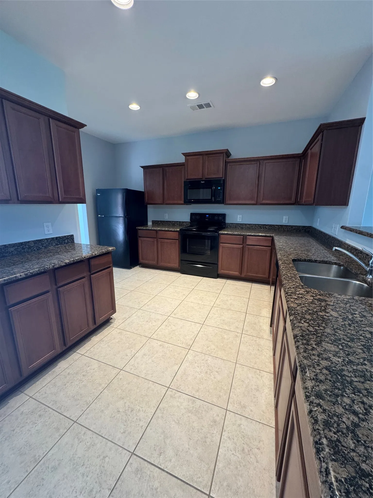 Kitchen featuring dark wood cabinetry, granite-style countertops, stainless steel double basin sink, black appliances, and recessed lighting