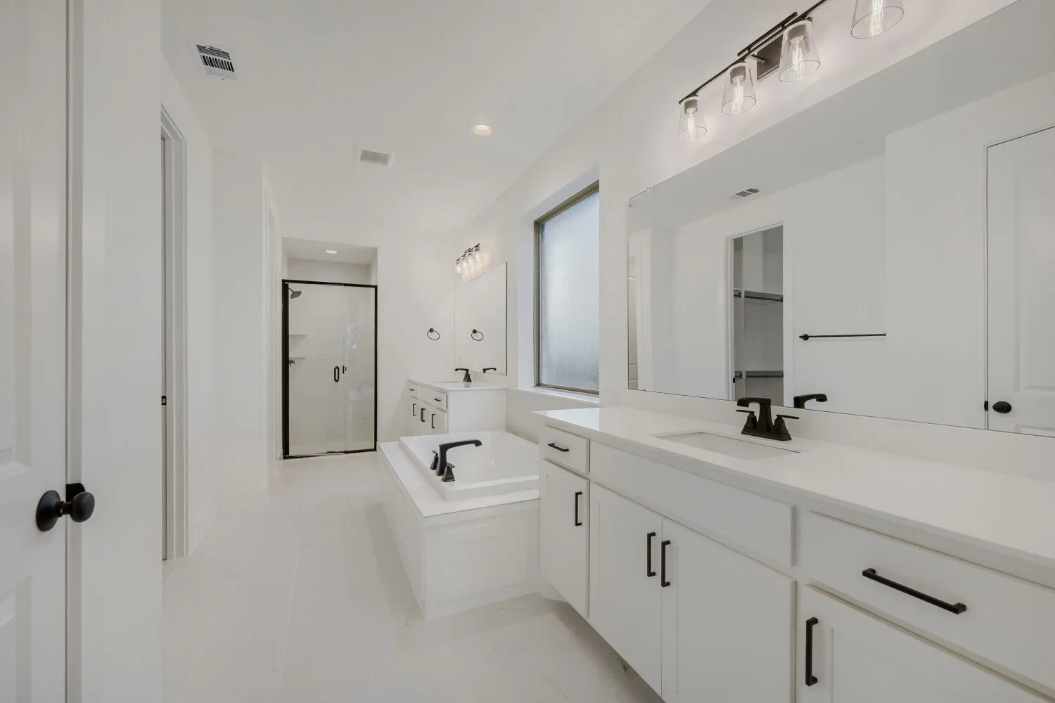 White bathroom featuring a glass-enclosed shower, a built-in soaking tub with black fixtures, and a dual vanity with white cabinetry and countertops