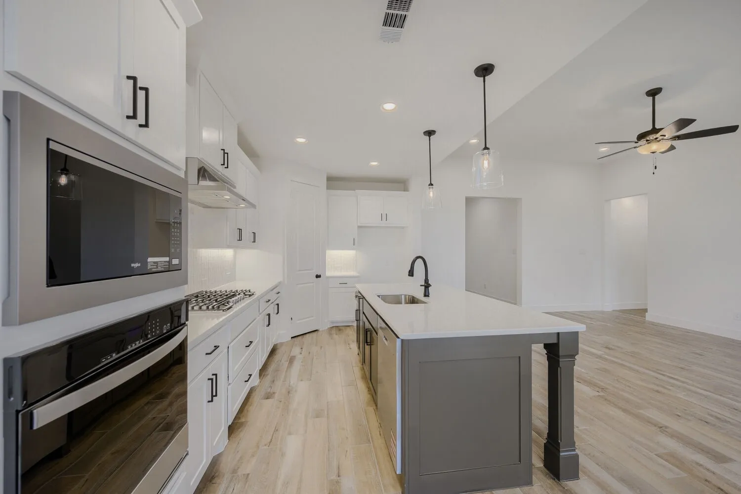 Modern kitchen featuring white cabinetry, stainless steel appliances, a center island with a sink, pendant lighting, and wood-finish flooring
