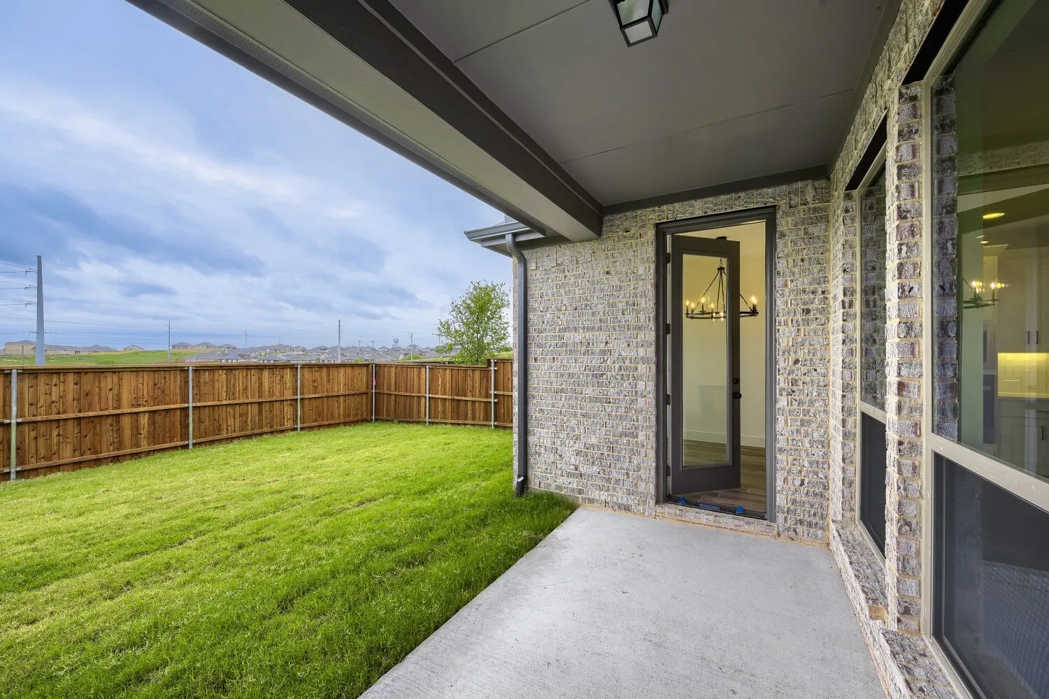 Covered patio with a concrete surface, light-toned brick exterior, and a glass-paned door