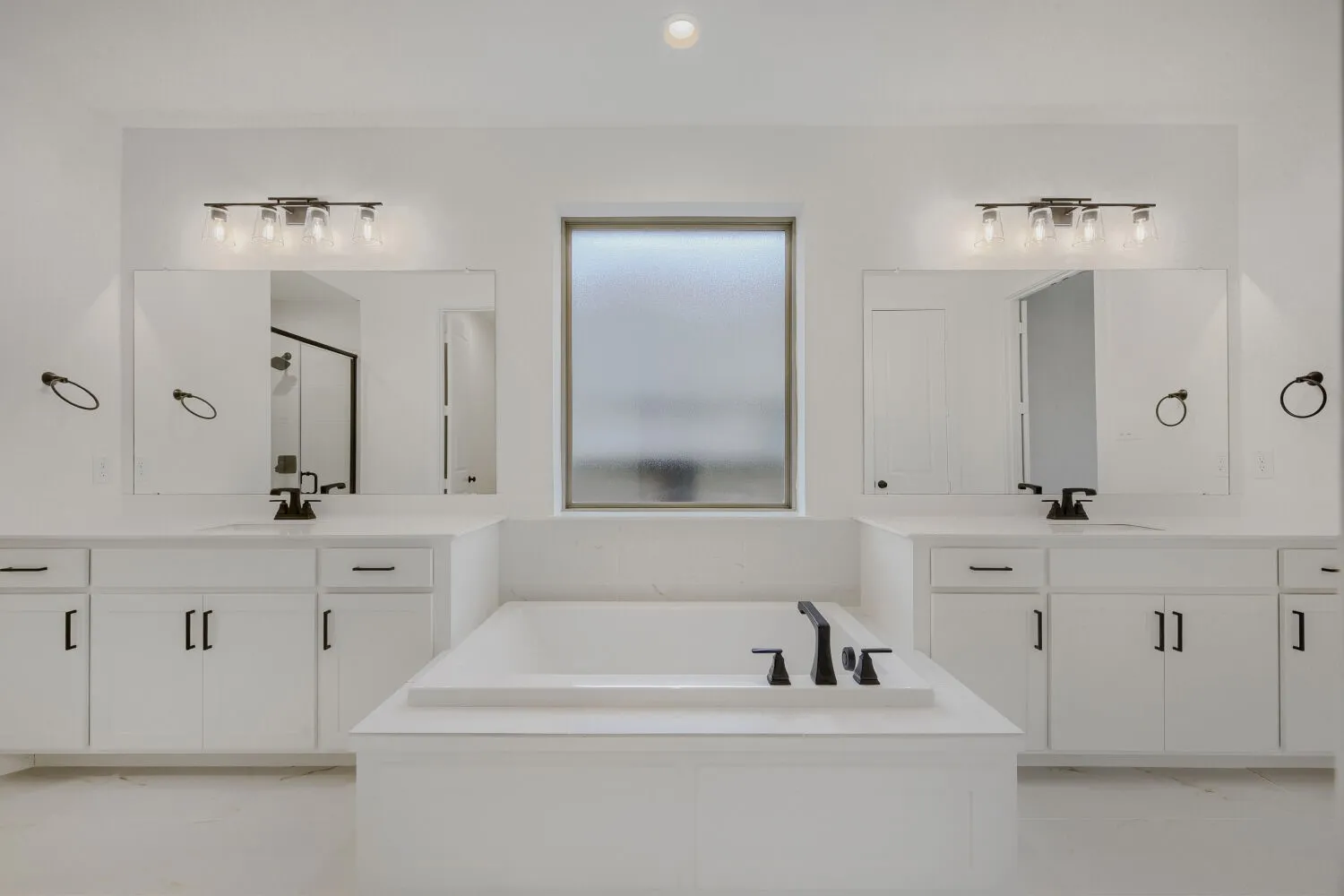 Bathroom featuring a built-in tub, dual vanities with white cabinetry, quartz countertops, and matte black fixtures