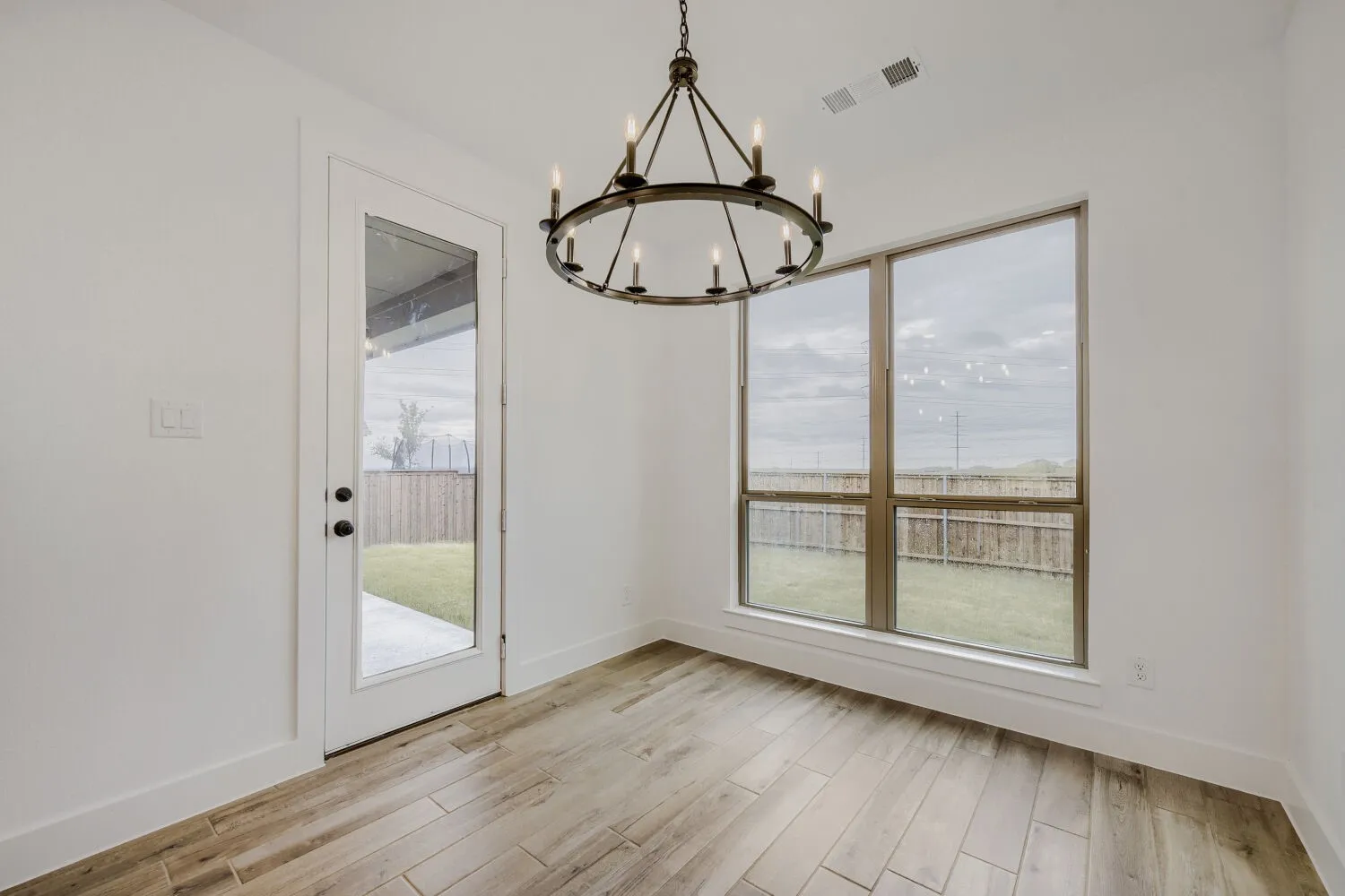 Bright interior space featuring a dark bronze chandelier, wood-finish flooring, and large picture windows
