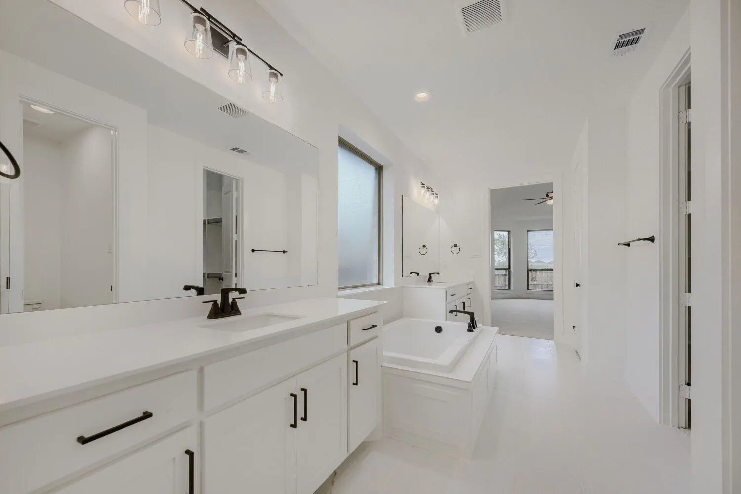 Spacious bathroom featuring dual vanities with white cabinetry and countertops, a large soaking tub with matte black fixtures, and modern overhead lighting
