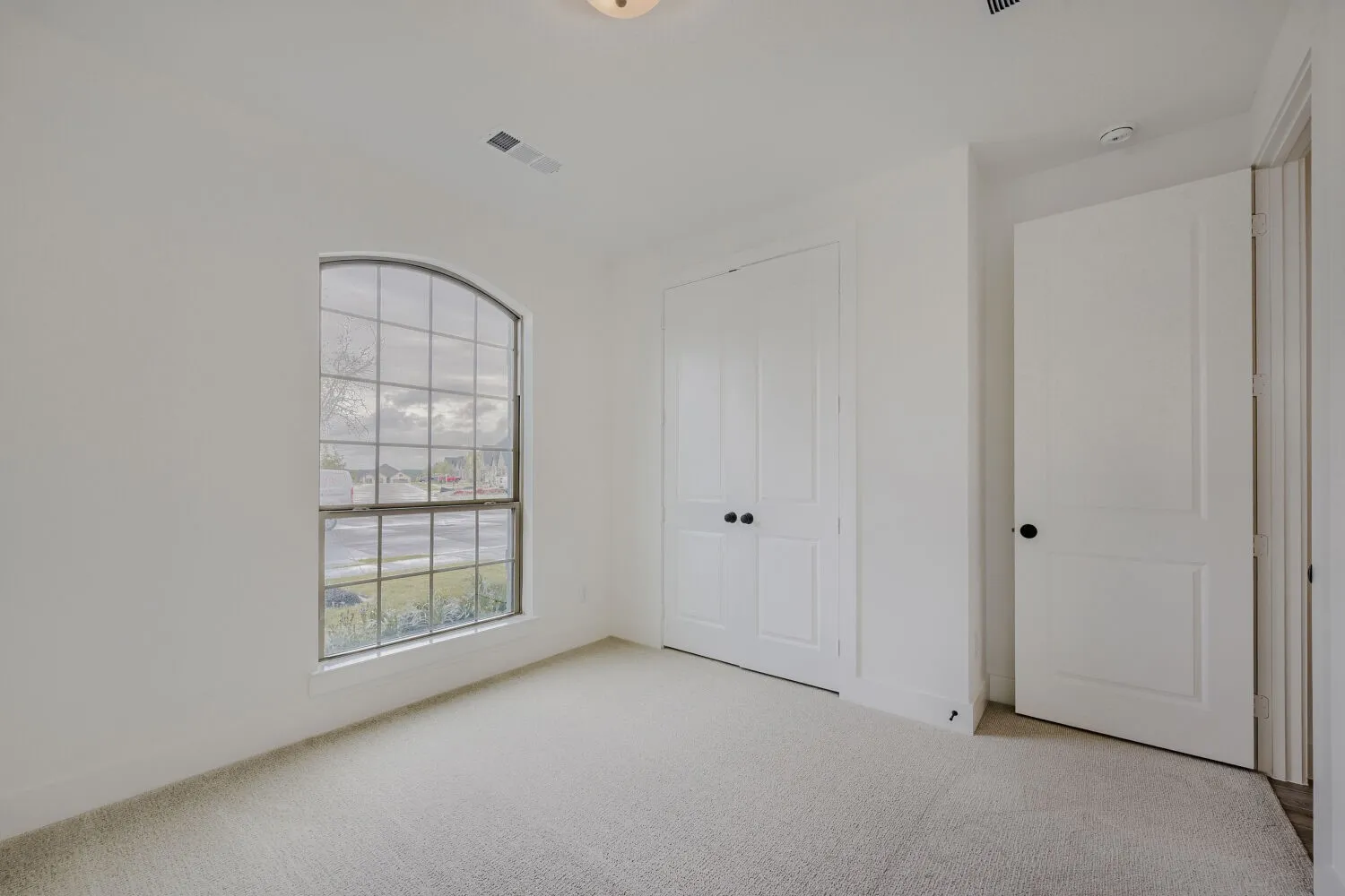 Room featuring light-colored carpeting, an arched window, white walls, and a pair of white bifold doors