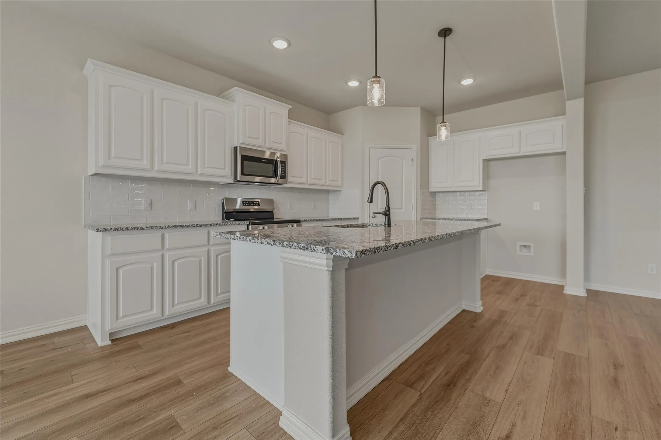 Kitchen featuring an island, white cabinetry, integrated stainless steel microwave, wood-finish flooring, and pendant lighting