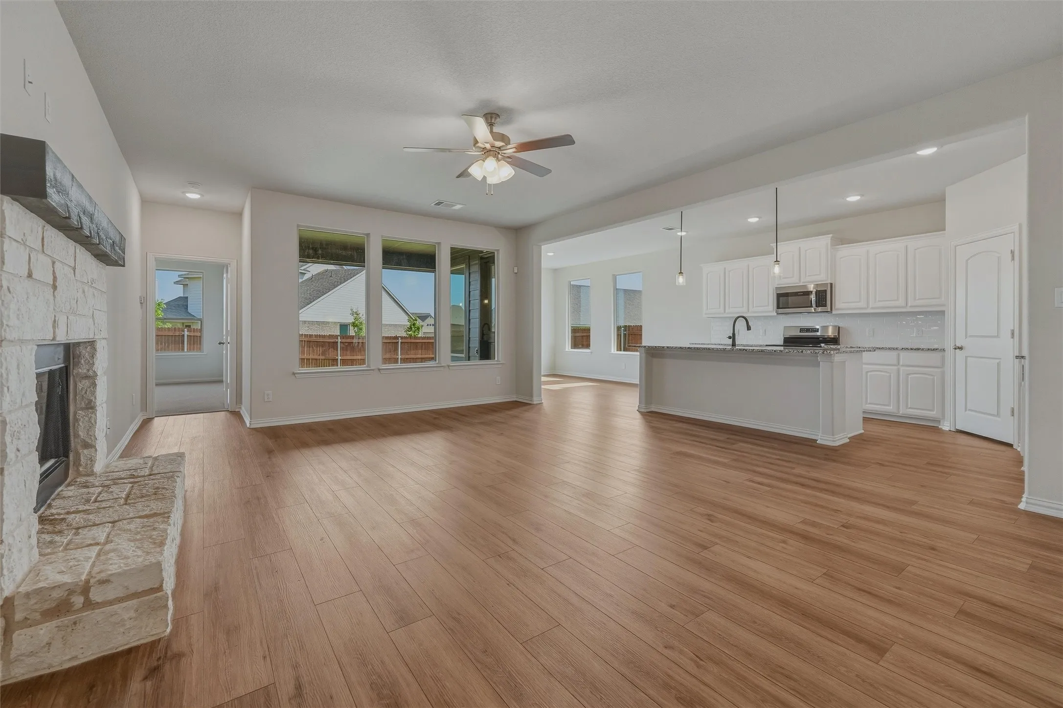 Spacious living area featuring wood-finish flooring, a stone-clad fireplace with a wood mantel, and multiple windows