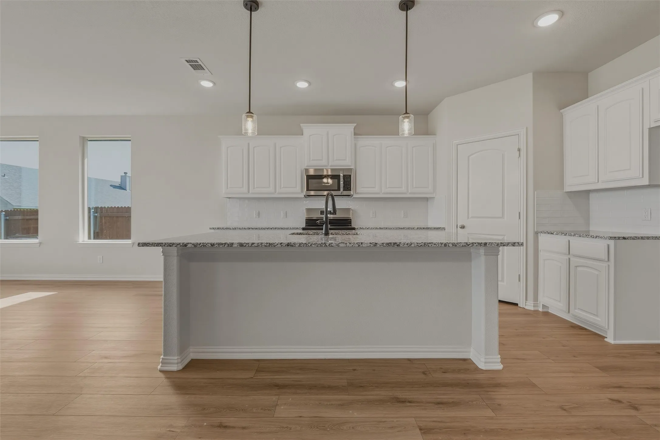 Kitchen featuring wood-finish flooring, white cabinetry, granite countertops, and a subway tile backsplash
