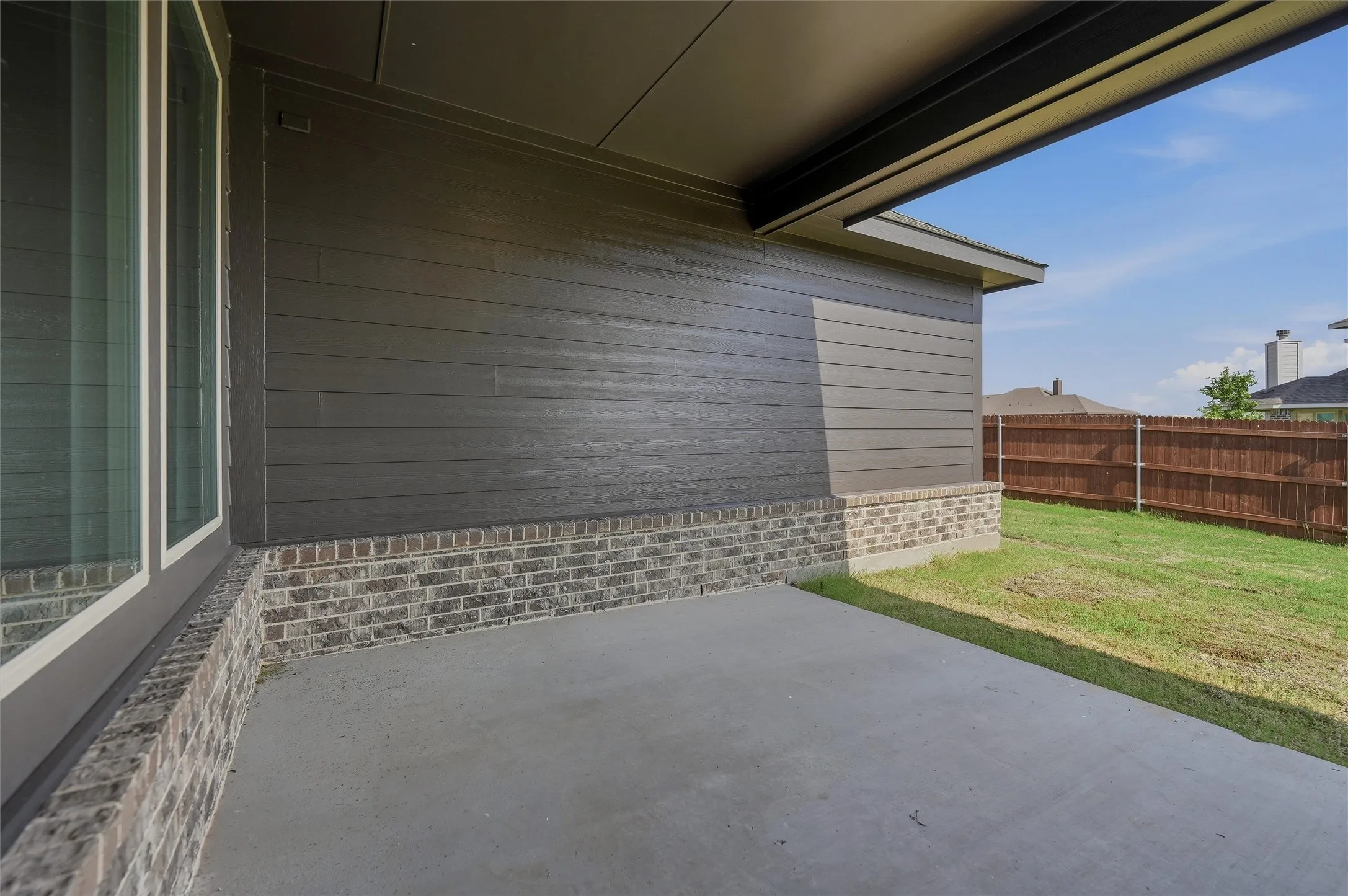 Covered outdoor patio with a concrete slab, board and batten siding, brick wainscoting, and a wood privacy fence