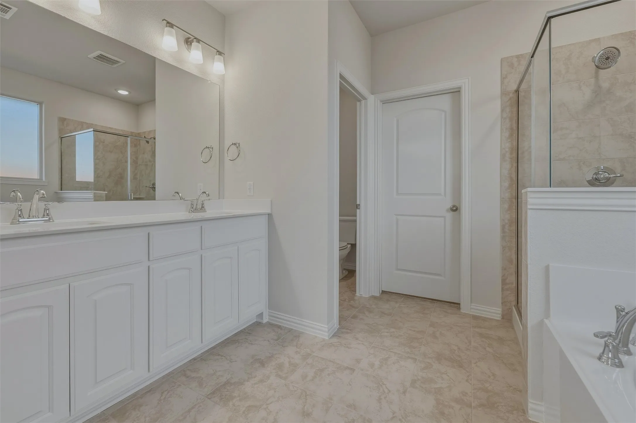 Dual vanity with white cabinetry, tile flooring, glass-enclosed shower, and a built-in tub