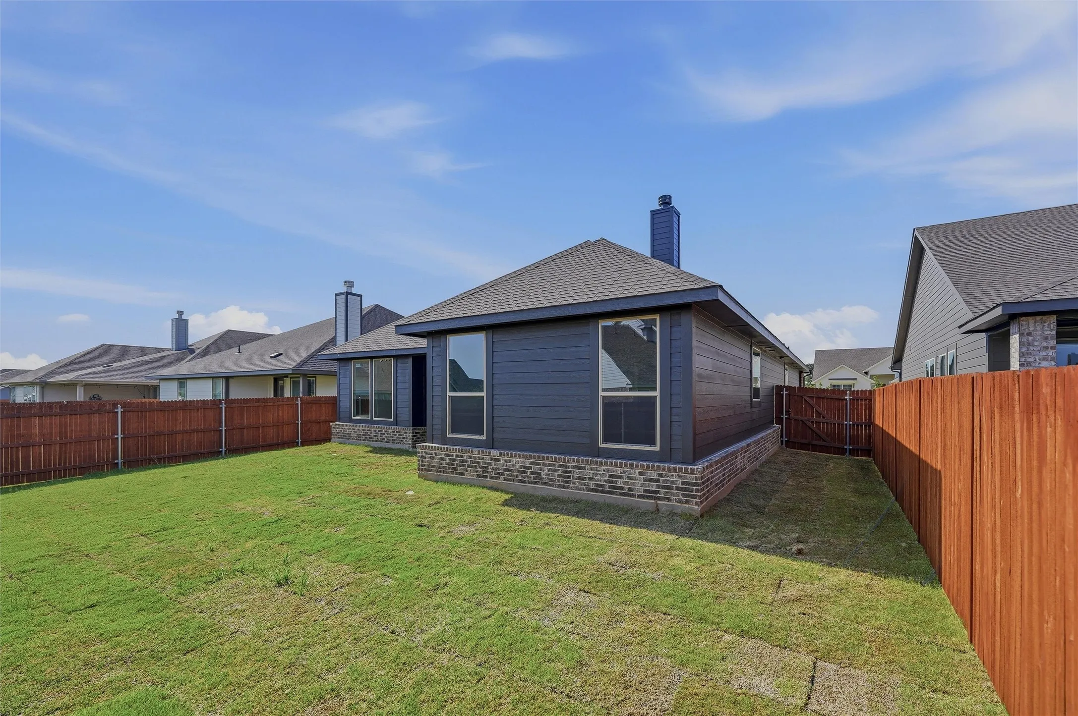 Manicured lawn, full privacy fencing, dark siding, brick accents, and a shingle roof