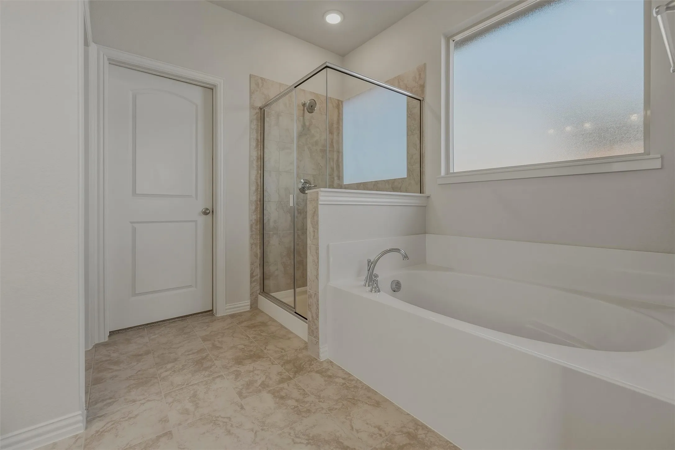 Spa-inspired primary bathroom featuring a freestanding soaking tub with deck-mounted faucet, a walk-in shower enclosure with frameless glass panels and tile surround, neutral tile flooring, soft ambient lighting, and a large window providing natural light