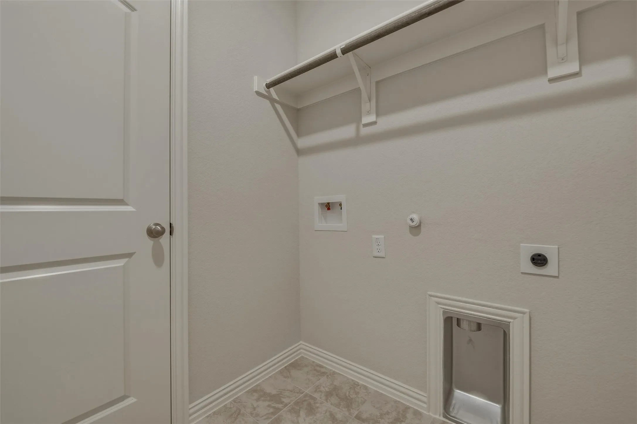 Laundry area with tile flooring, wall shelving, and a hanging rod