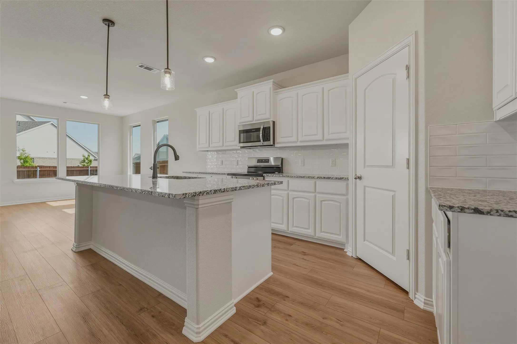 Kitchen featuring an island with stone countertops, white cabinetry, integrated stainless steel appliances, a subway tile backsplash, and wood-finish flooring