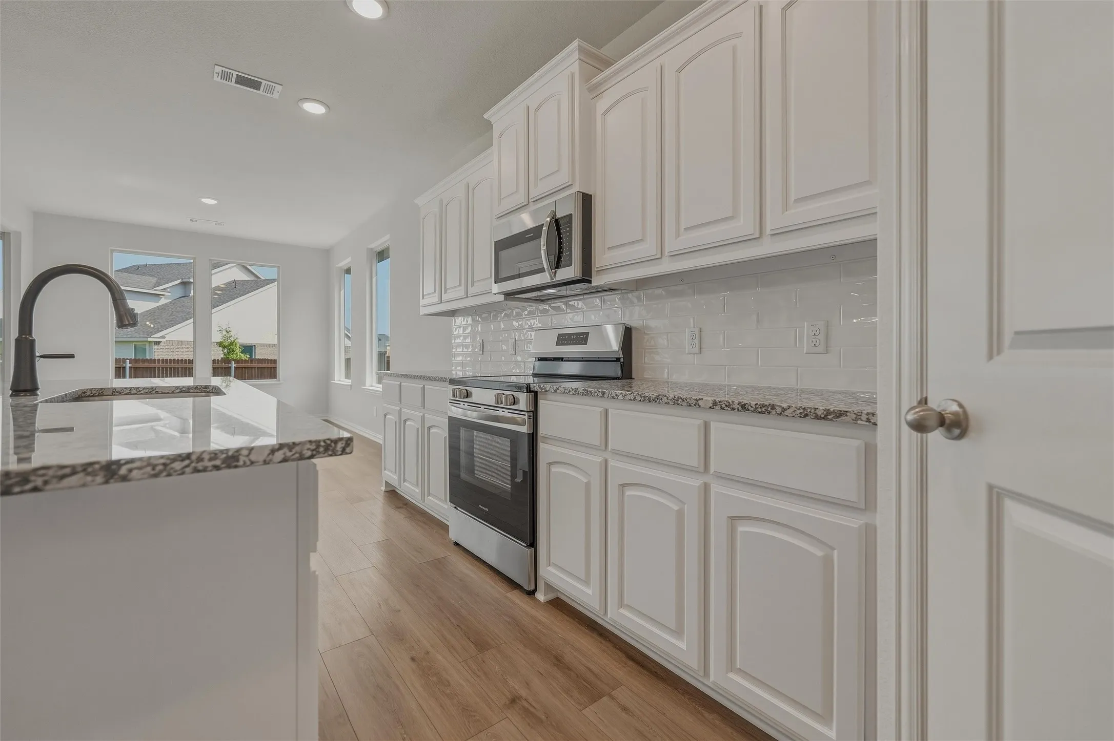 Kitchen featuring white cabinetry, granite countertops, stainless steel appliances, a tiled backsplash, and wood-finish flooring