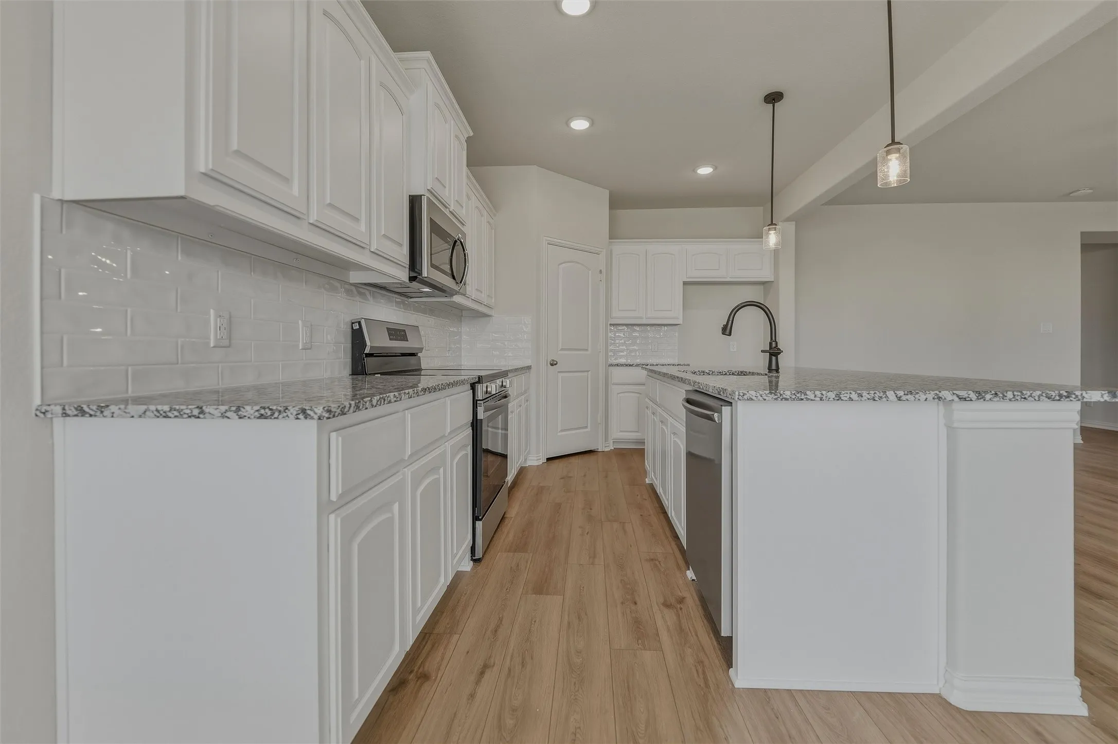 Kitchen featuring wood-finish flooring, white cabinetry, a tile backsplash, and stone countertops