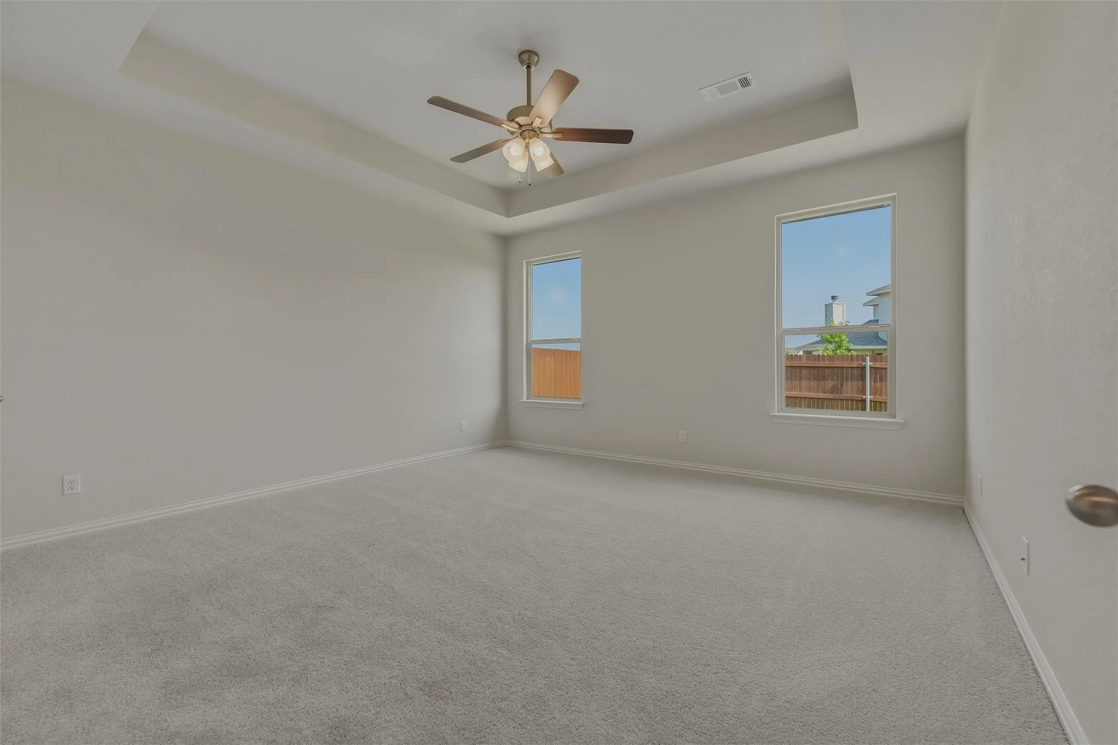 Spacious room featuring a tray ceiling, ceiling fan, two windows, and light gray carpet