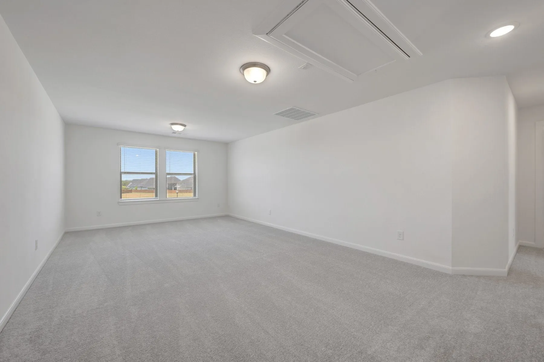Spacious room featuring light gray carpeting, neutral wall finishes, and two windows providing external visibility