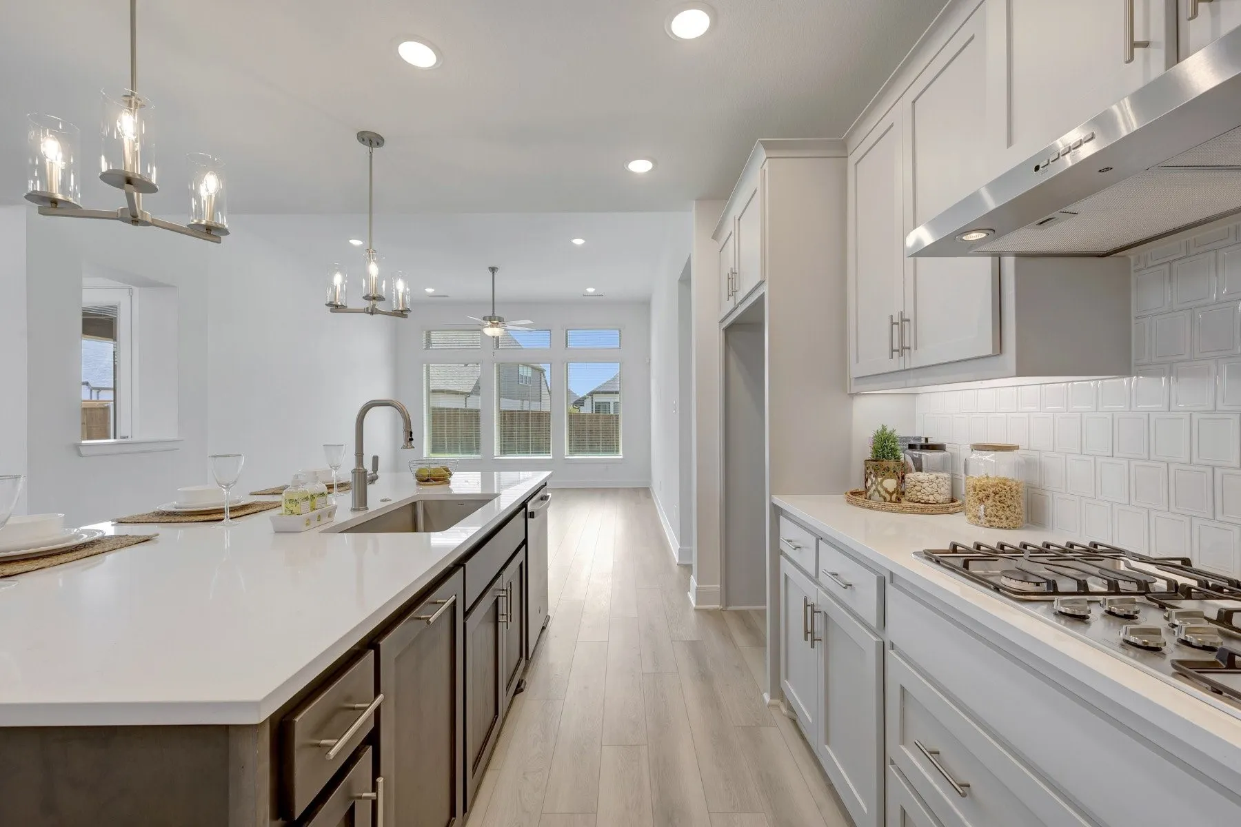 Contemporary kitchen featuring light wood-finish flooring, white cabinetry, integrated stainless steel appliances, a gas cooktop, and a spacious island with an undermount sink