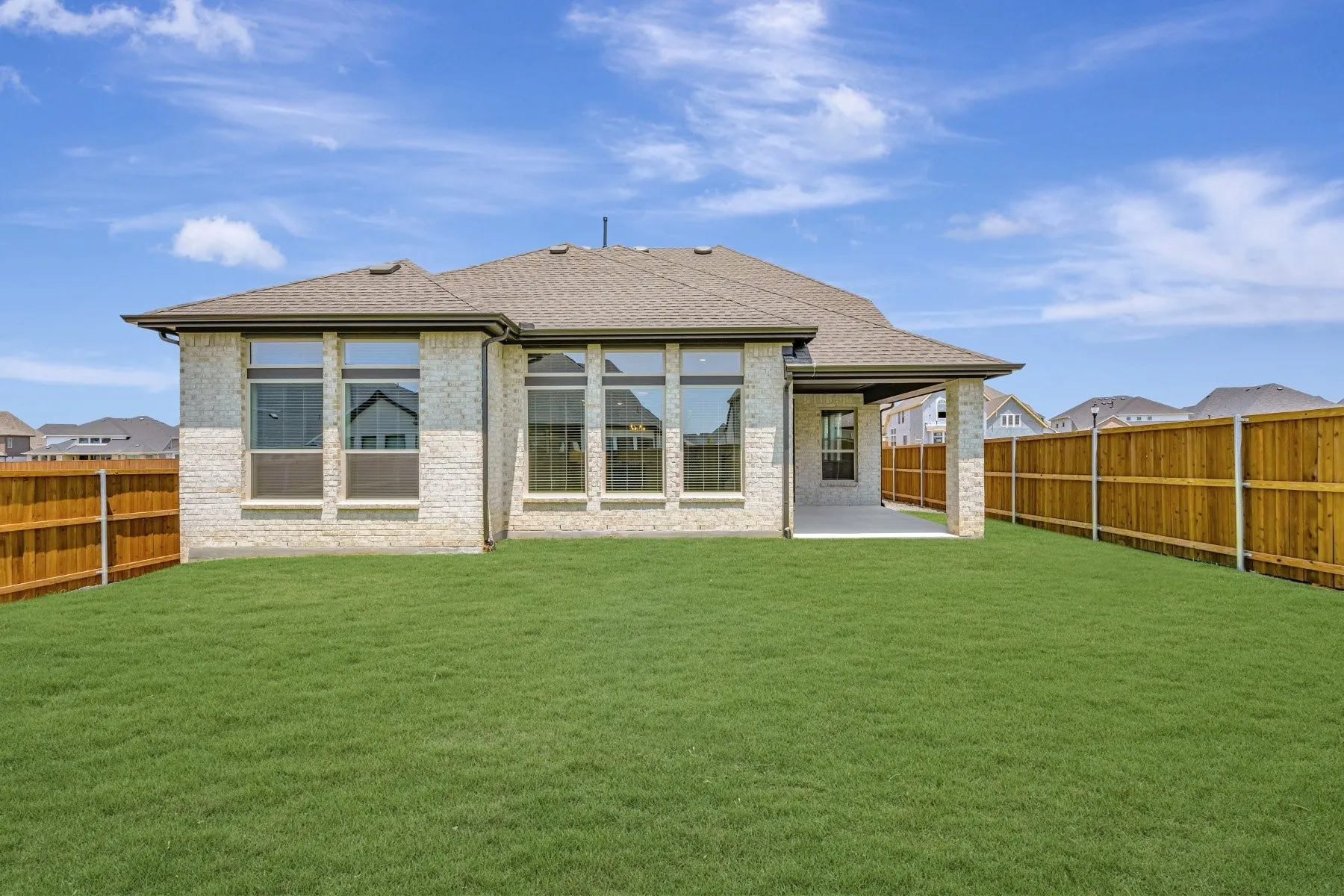 Expansive backyard with a manicured lawn, full privacy fencing, and a covered concrete patio
