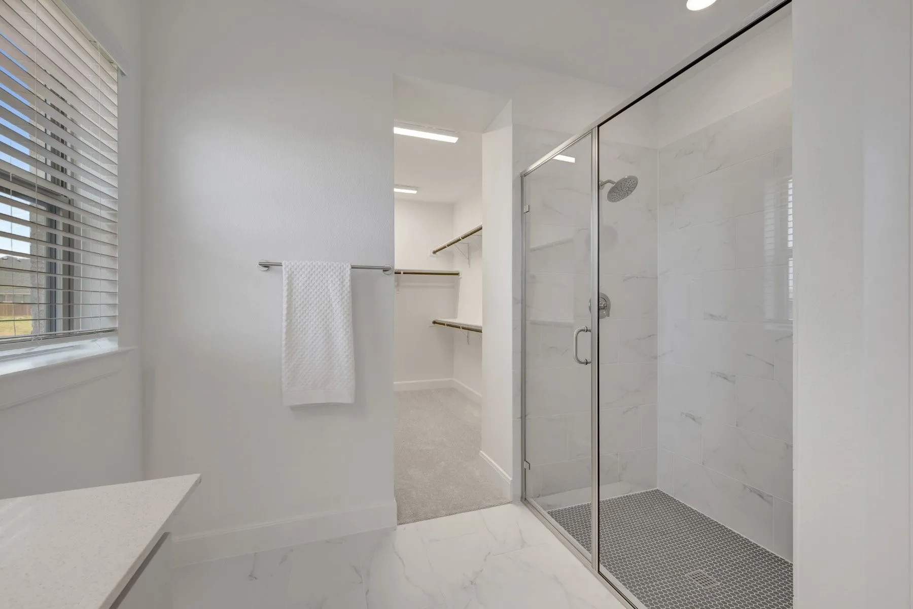 Walk-in shower with clear glass enclosure and white marble-look tile surround